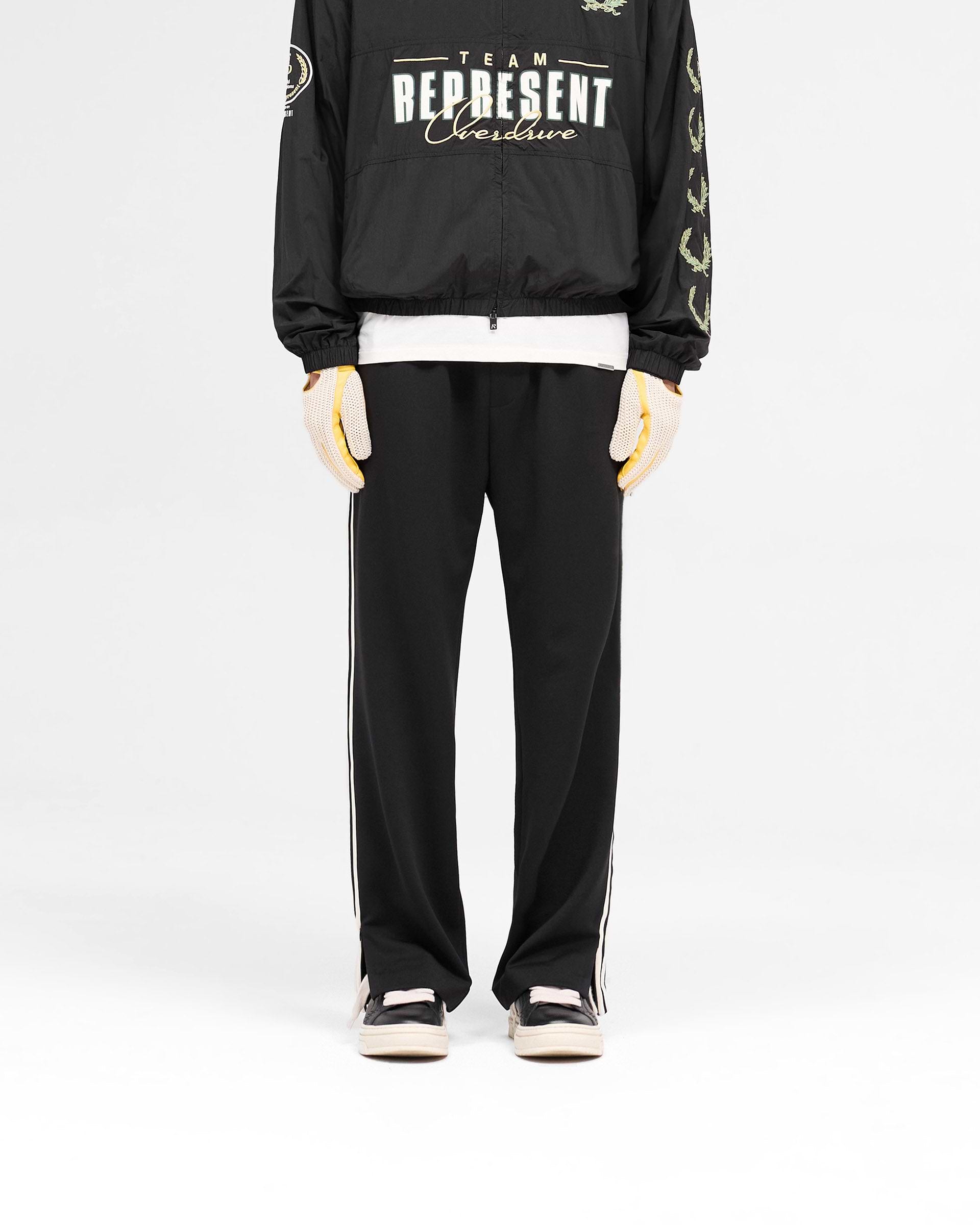 Man wearing tailored black pants on a plain white background | Tailored Track Pant in Jet Black | Pants with elasticated waistband and zip detailing | SS25 Pants | Represent Clo