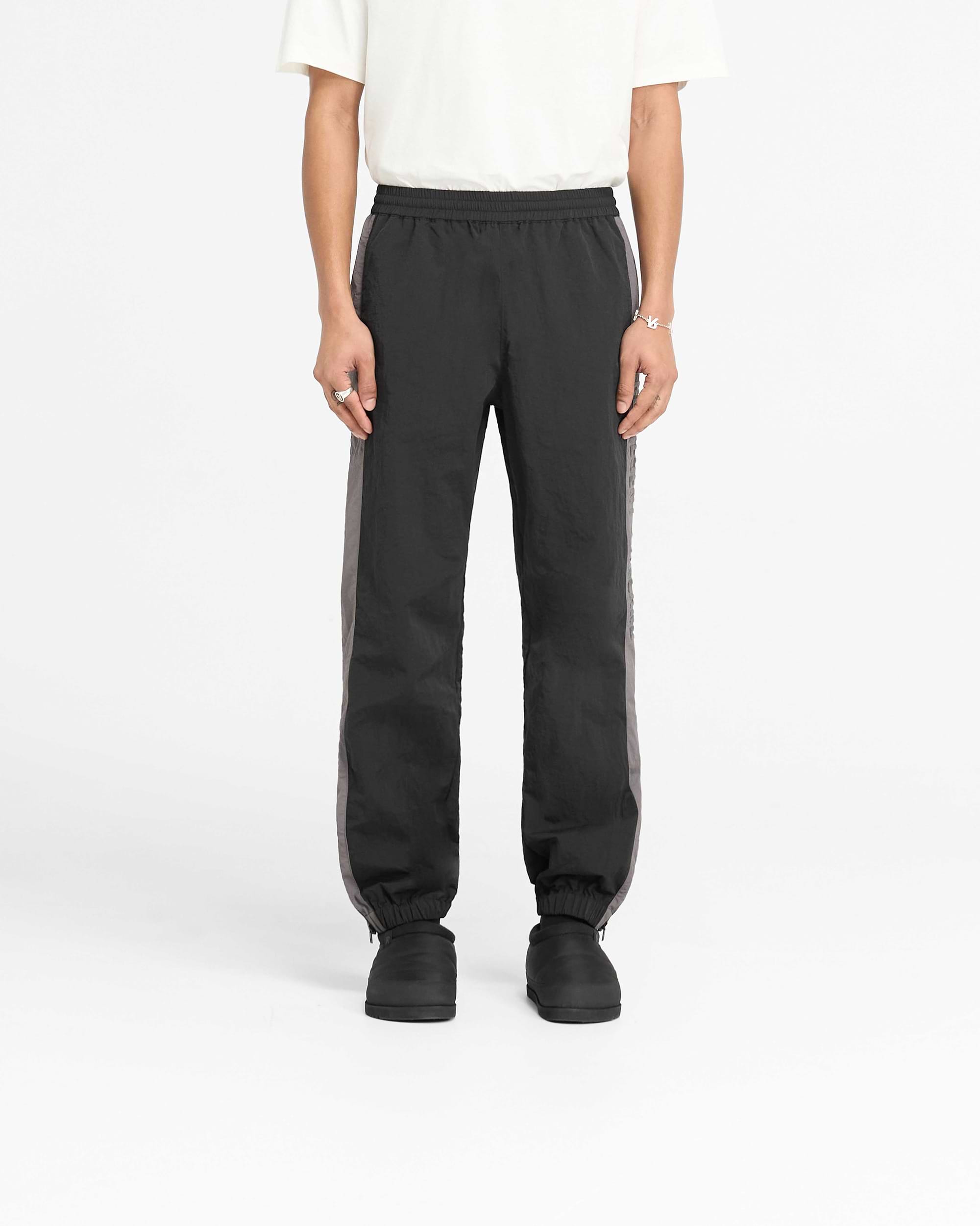 Man wearing black nylon track pants on a plain white background | Nylon Track Pant in Black | Track pants with elasticated waistband and hem zip | PRE SS25 Pants | Represent Clo