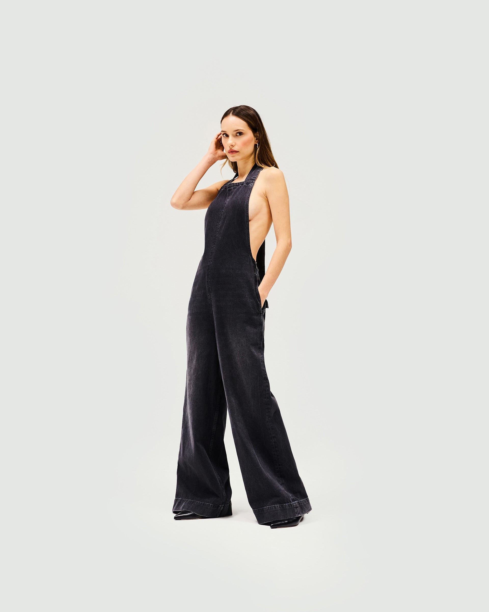 Woman wearing a black denim jumpsuit on a plain white background | Voltage Denim Jumpsuit in Washed Black | Statement denim jumpsuit with wide leg and XL long back tie | Womens SS25 Denim | Represent Clo