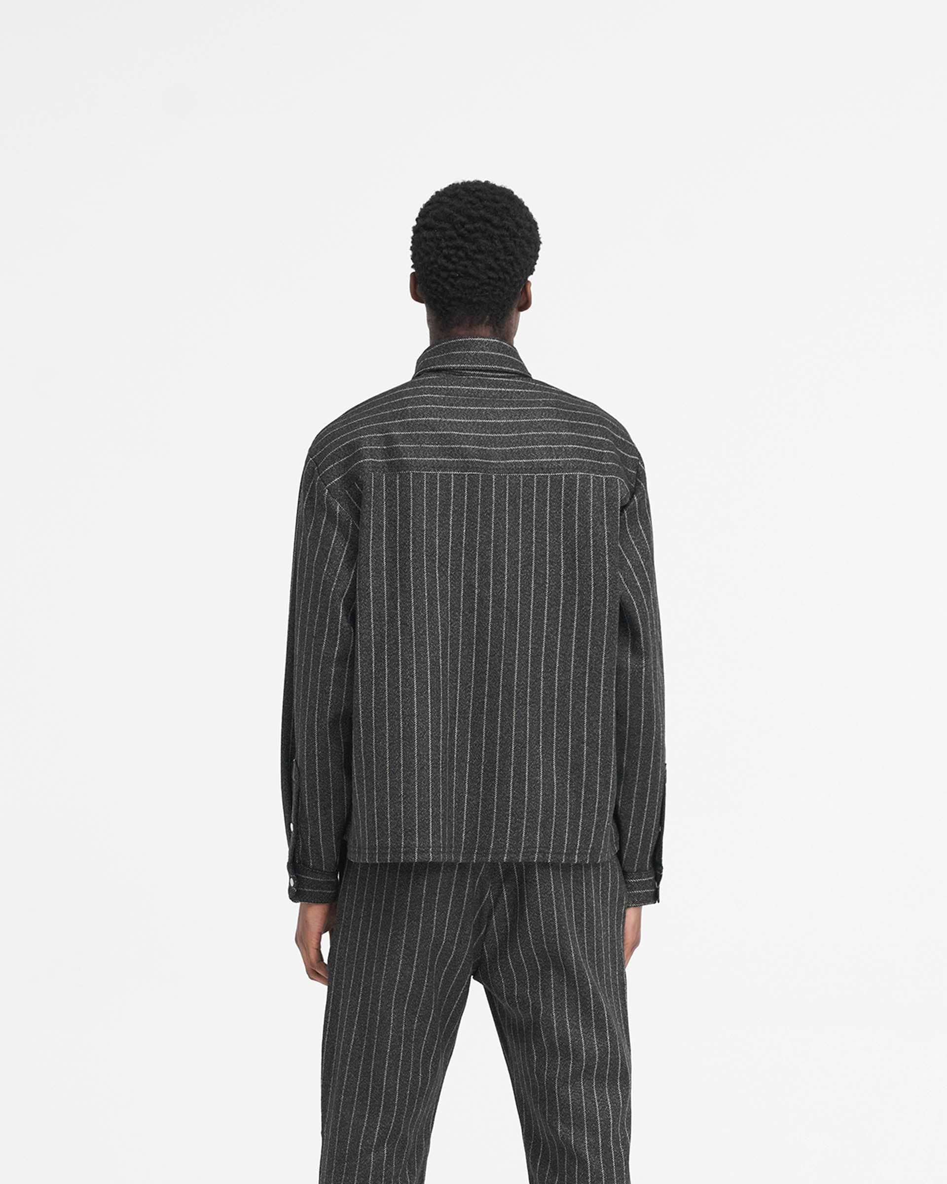 Man wearing a black pinstripe cropped dress shirt on a plain white background | Cropped Dress Shirt in Black Pinstripe | Dress shirt with stepped hem and antique silver logo | SS24 Shirts | Represent Clo