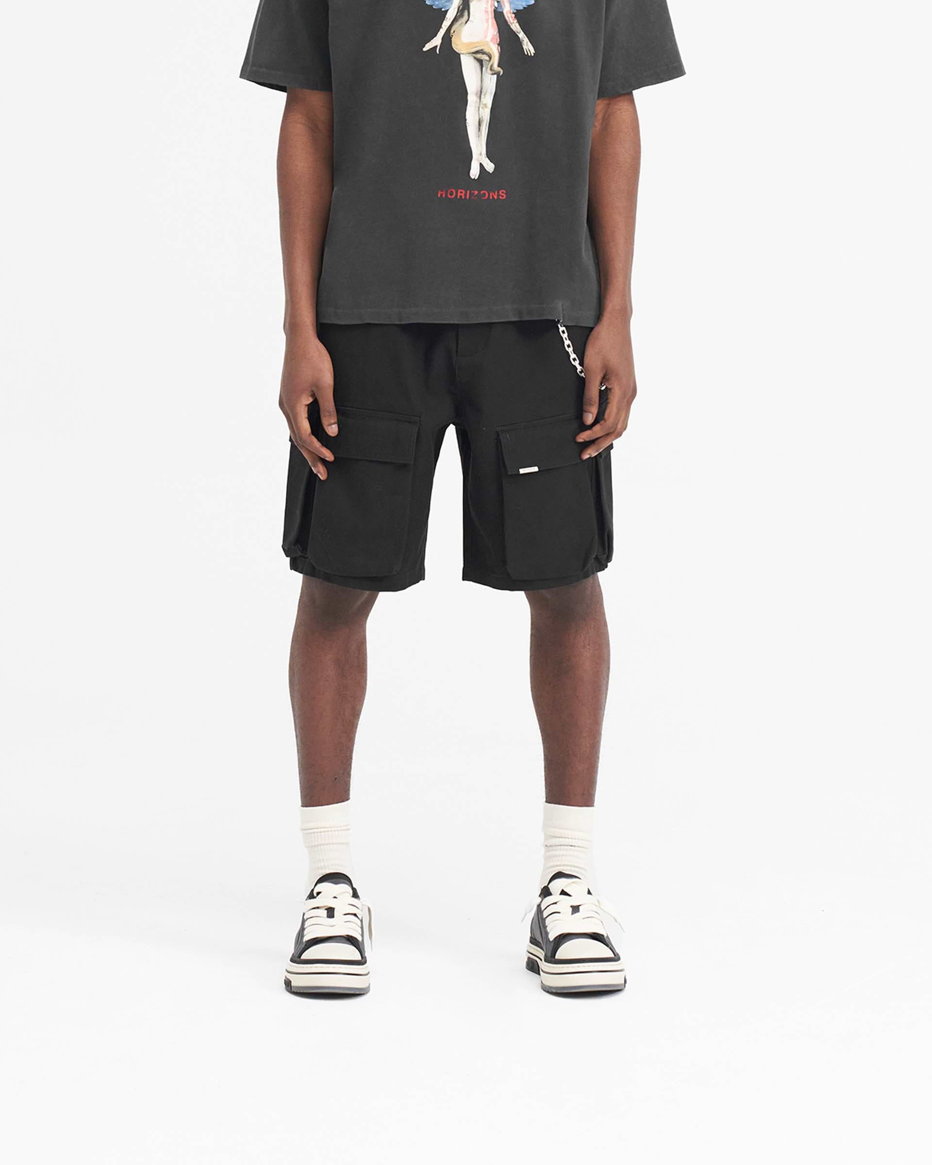 Man wearing black baggy cotton cargo shorts on a plain white background | Baggy Cotton Cargo Short in Black | Baggy fit shorts with 3D pockets | SS24 Shorts | Represent Clo