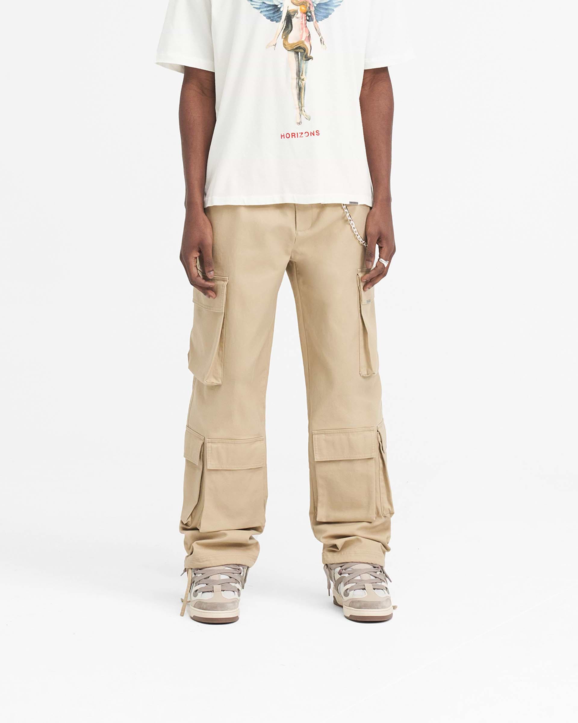 Man wearing baggy beige cargo pants on a plain white background | Baggy Cargo Pant in Sandstone | Baggy fit with 3D oversized pockets | SS24 Pants | Represent Clo