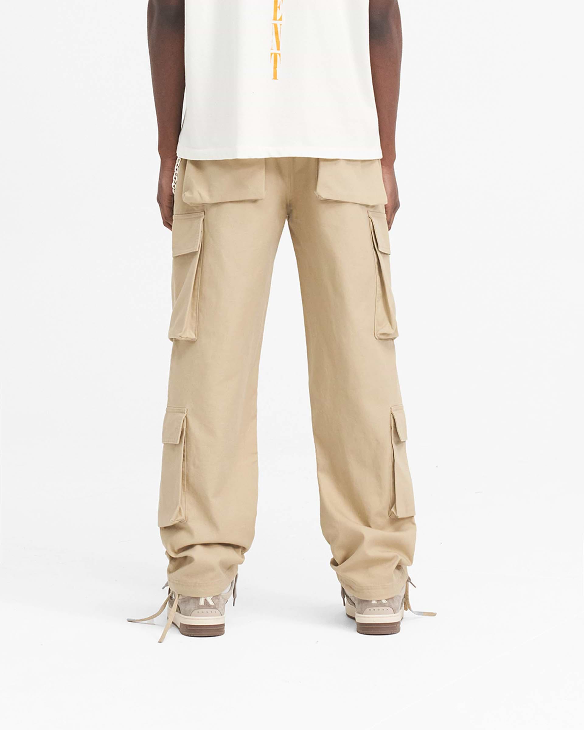 Man wearing baggy grey cargo pants on a plain white background | Baggy Cargo Pant in Sandstone | Cargo pants with 3D oversized pockets and antique silver hardware | SS24 Pants | Represent Clo