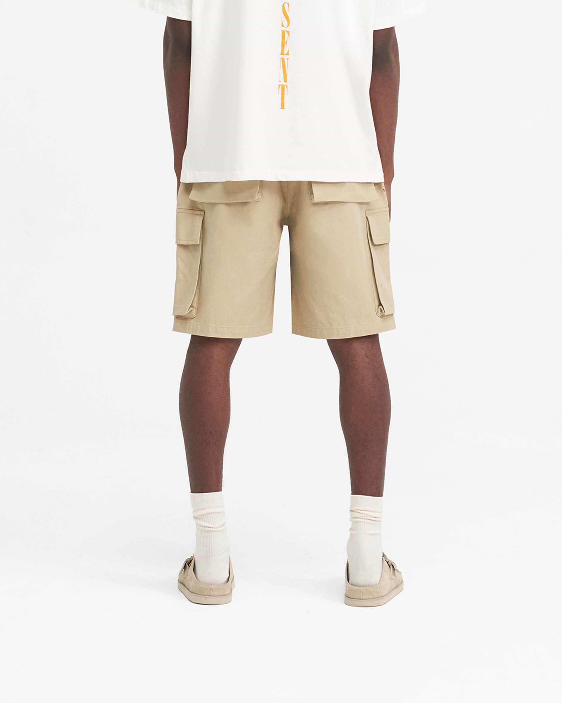 Man wearing baggy cotton cargo shorts in sandstone on a plain white background | Baggy Cotton Cargo Short in Sandstone | Cargo shorts with oversized 3D pockets | SS24 Shorts | Represent Clo