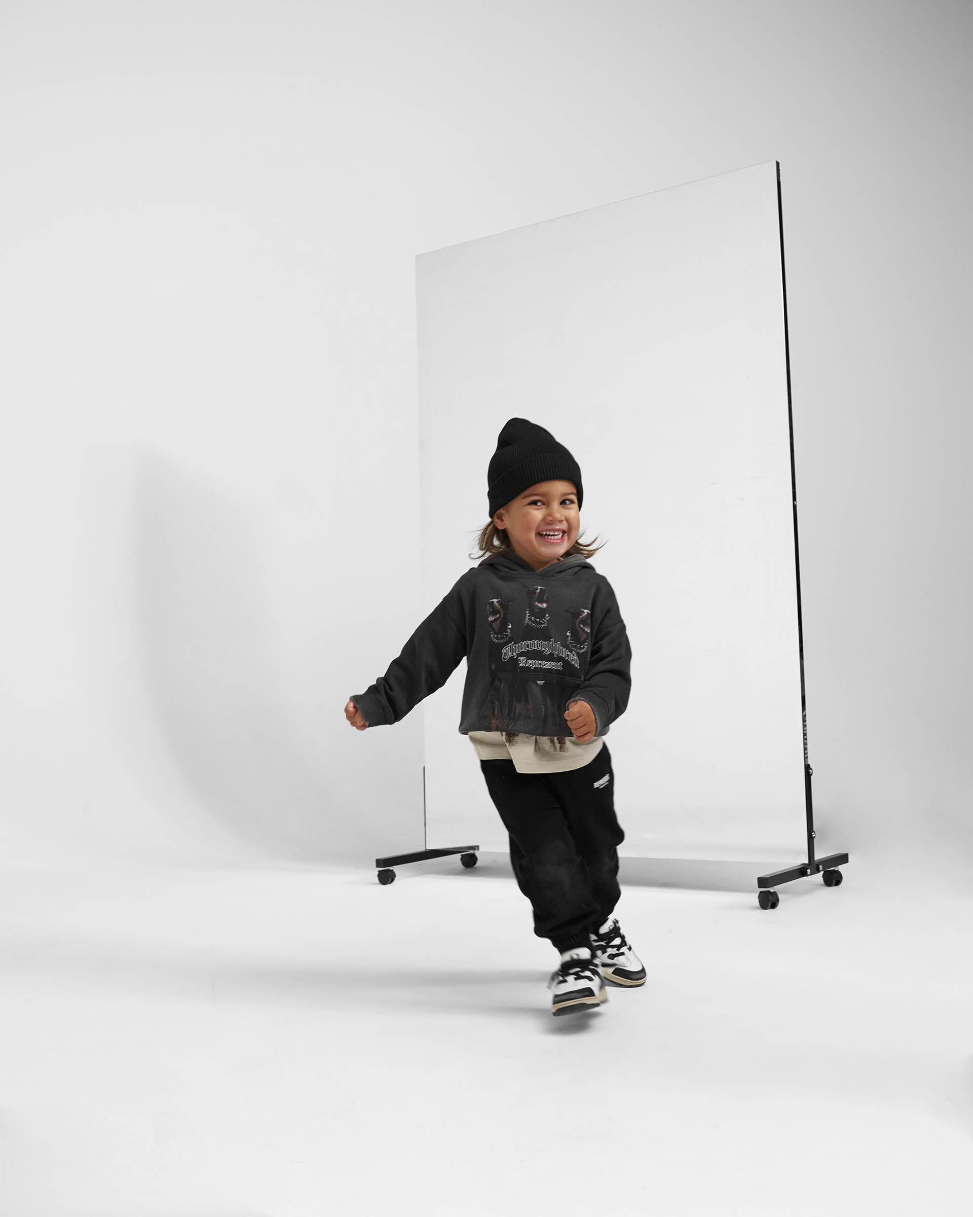 Child wearing a vintage black hoodie on a plain white background | Mini Thoroughbred Hoodie in Vintage Black | Kids oversized hoodie with graphic | Mini Hoodies | Represent Clo
