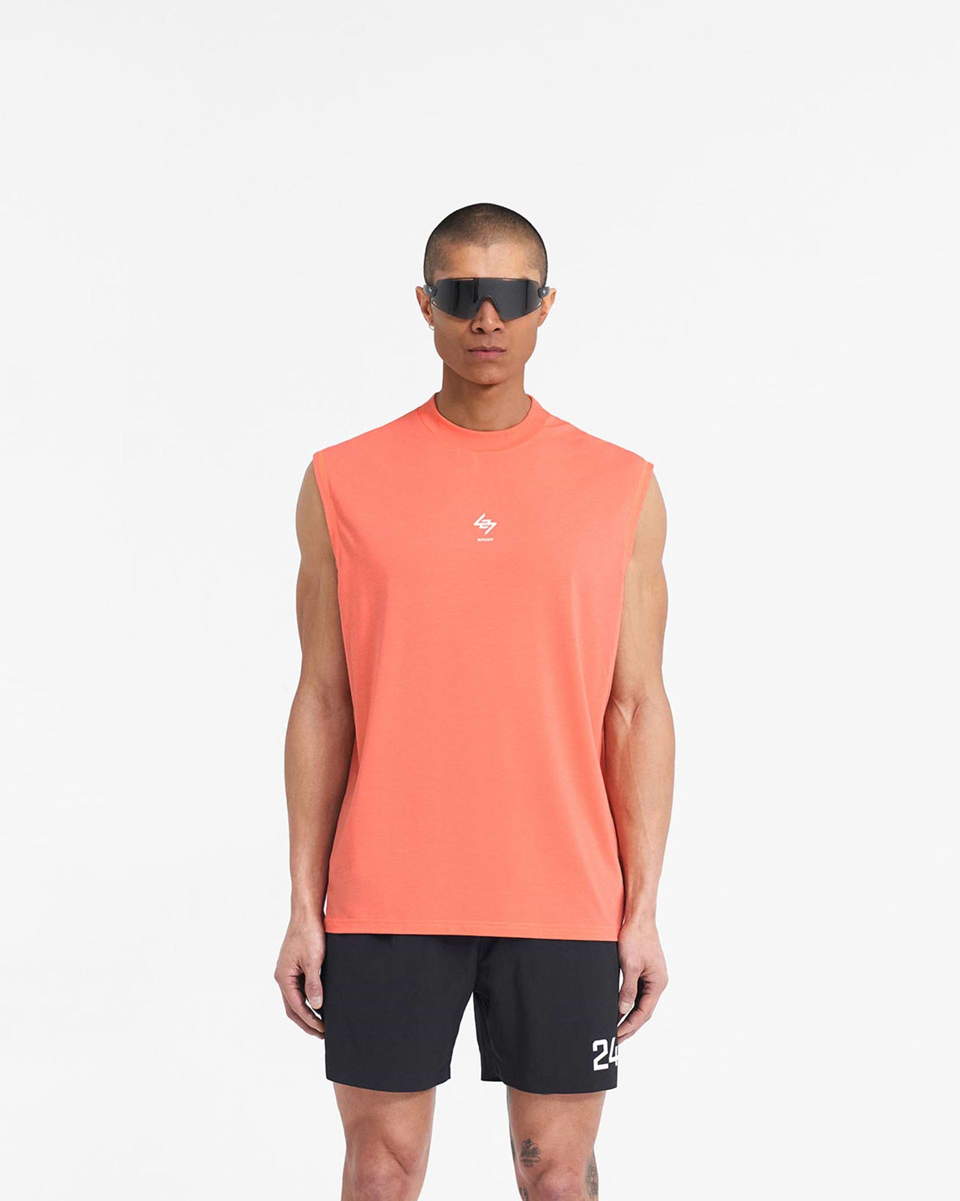 Man wearing a coral tank top on a plain white background | 247 Oversized Tank in Coral | Technical tank with breathable fabric and 247 branding | 247 T-Shirts | Represent Clo