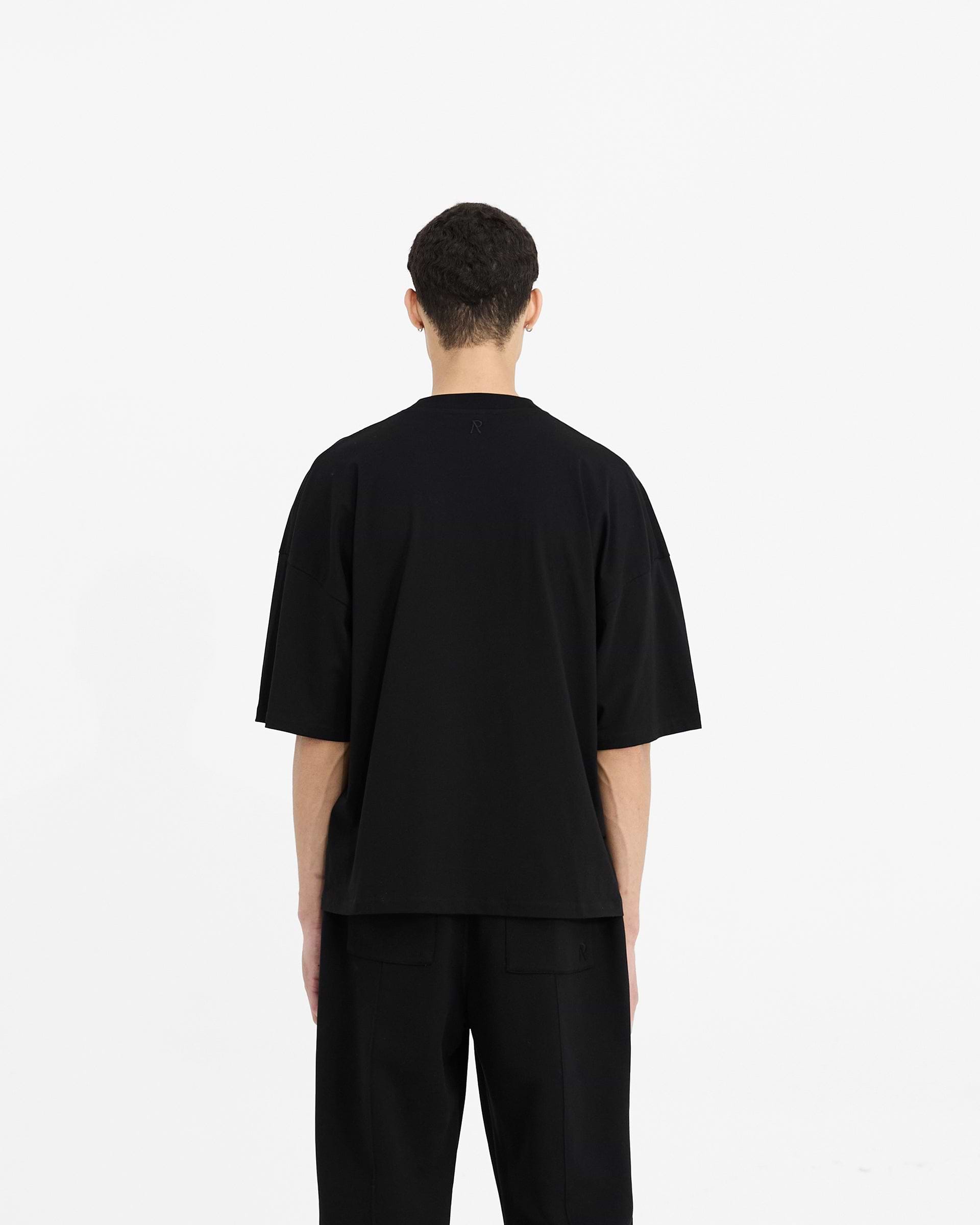 Man wearing an oversized black t-shirt on a plain white background | Initial Boxy T-Shirt in Black | Super oversized and boxy cropped t-shirt | Initial T-Shirts | Represent Clo