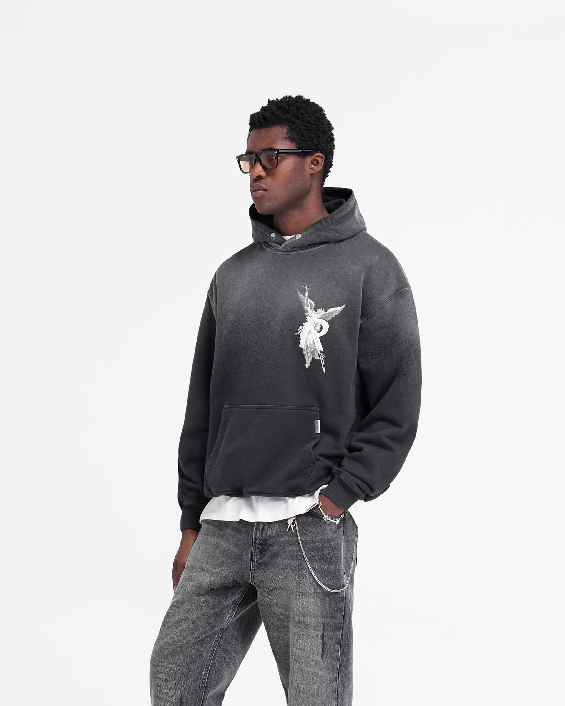 Man wearing a black hoodie with worn look on a plain white background | Archangel Hoodie in Stained Black | Oversized hoodie with high density graphic | FW24 Hoodies | Represent Clo