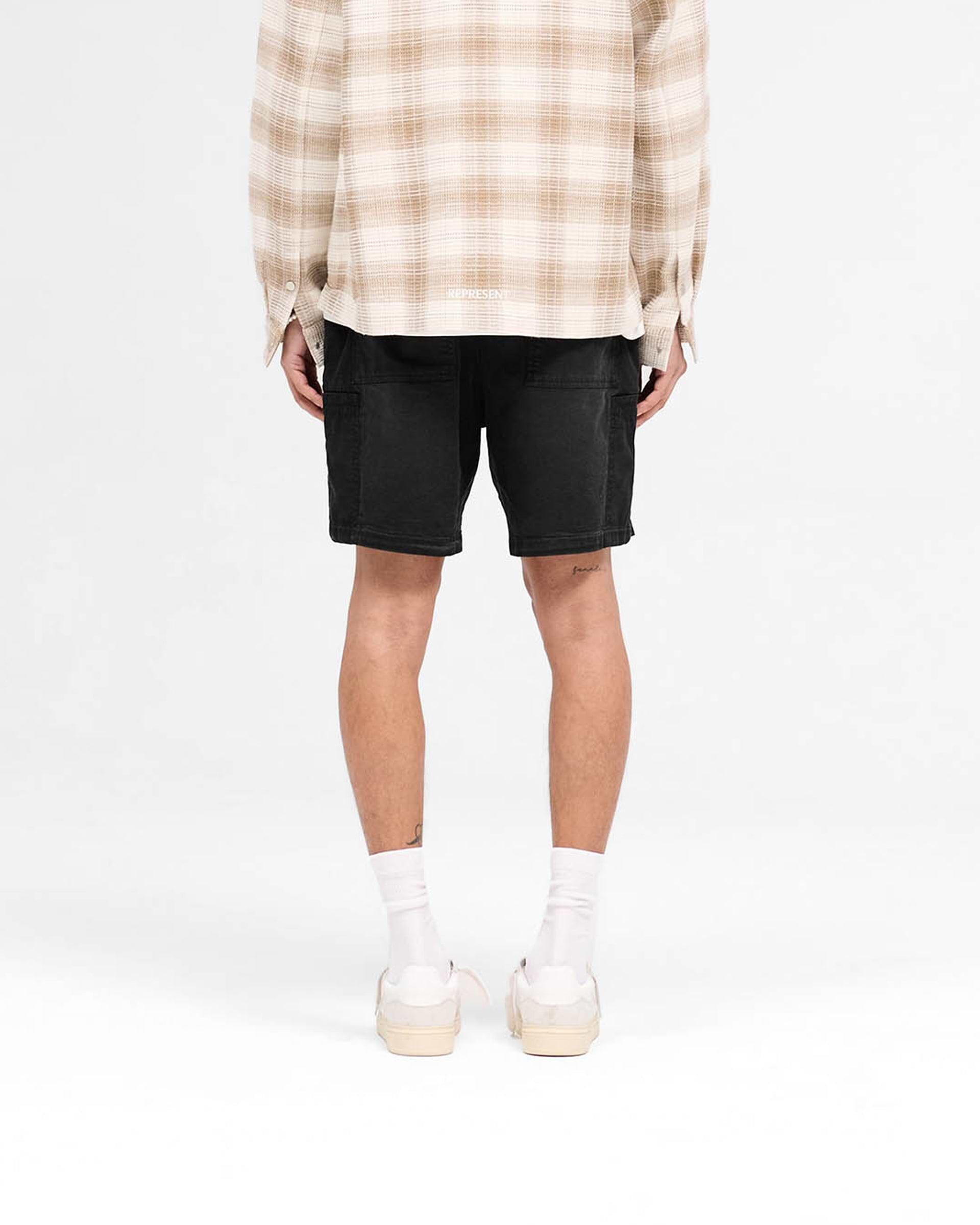 Man wearing black cargo shorts on a plain white background | Season Cargo Short in Jet Black | Brushed twill shorts with welt cargo pockets | SS25 Shorts | Represent Clo
