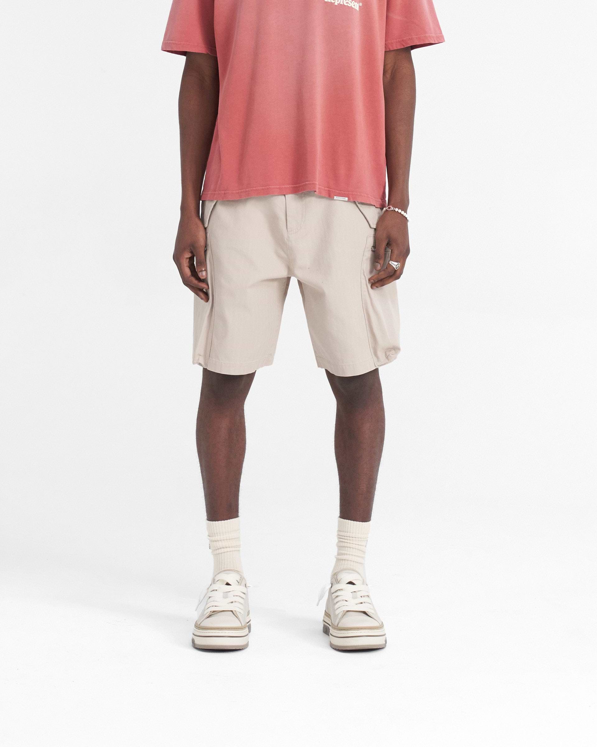 Man wearing cashmere beige shorts on a plain white background | Workshop Short in Cashmere | Baggy fit shorts with 3D back and cargo pockets | SS24 Shorts | Represent Clo