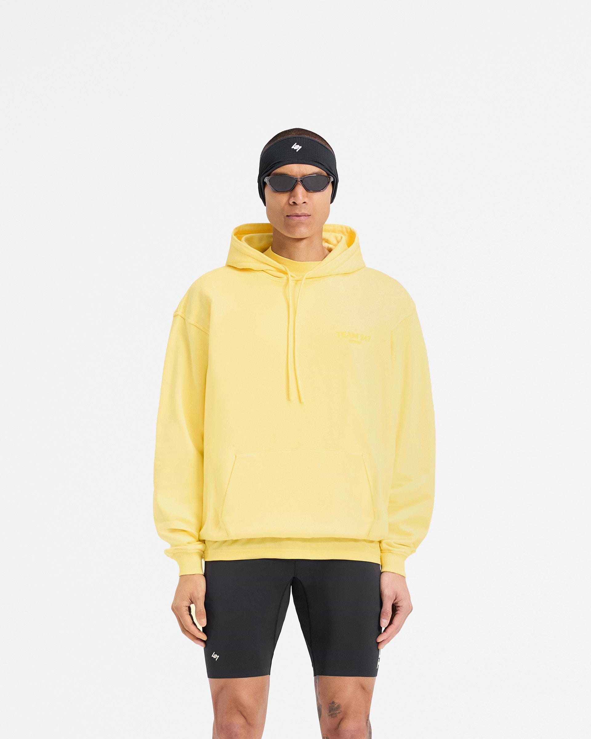 Man wearing a yellow hoodie on a plain white background | Team 247 Oversized Hoodie in Lemon | Oversized fit hoodie with Team 247 branding | 247 Hoodies | Represent Clo