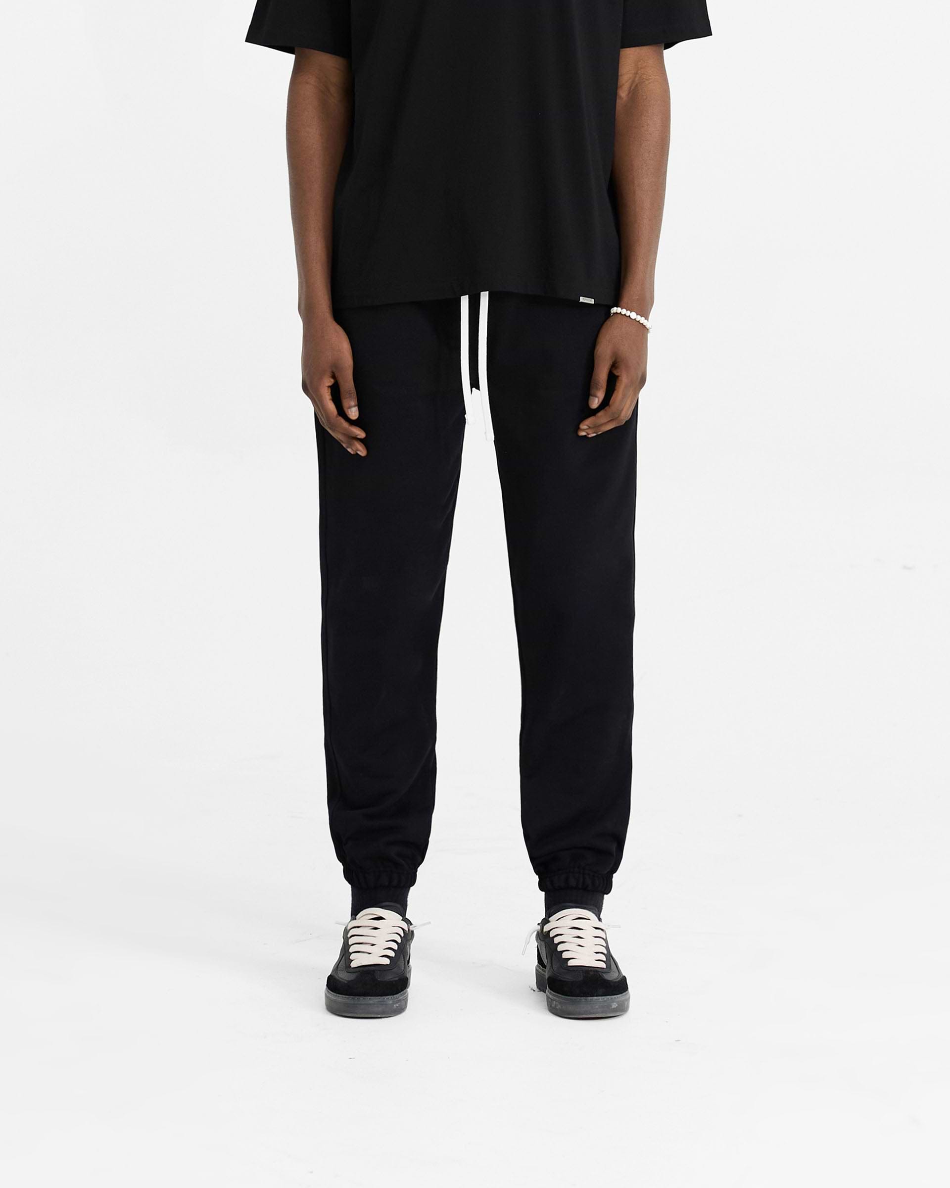 Man wearing black sweatpants on a plain white background | Initial Cuffed Sweatpant in Black | Sweatpants with elasticated waistband and cuffs | Initial Pants | Represent Clo