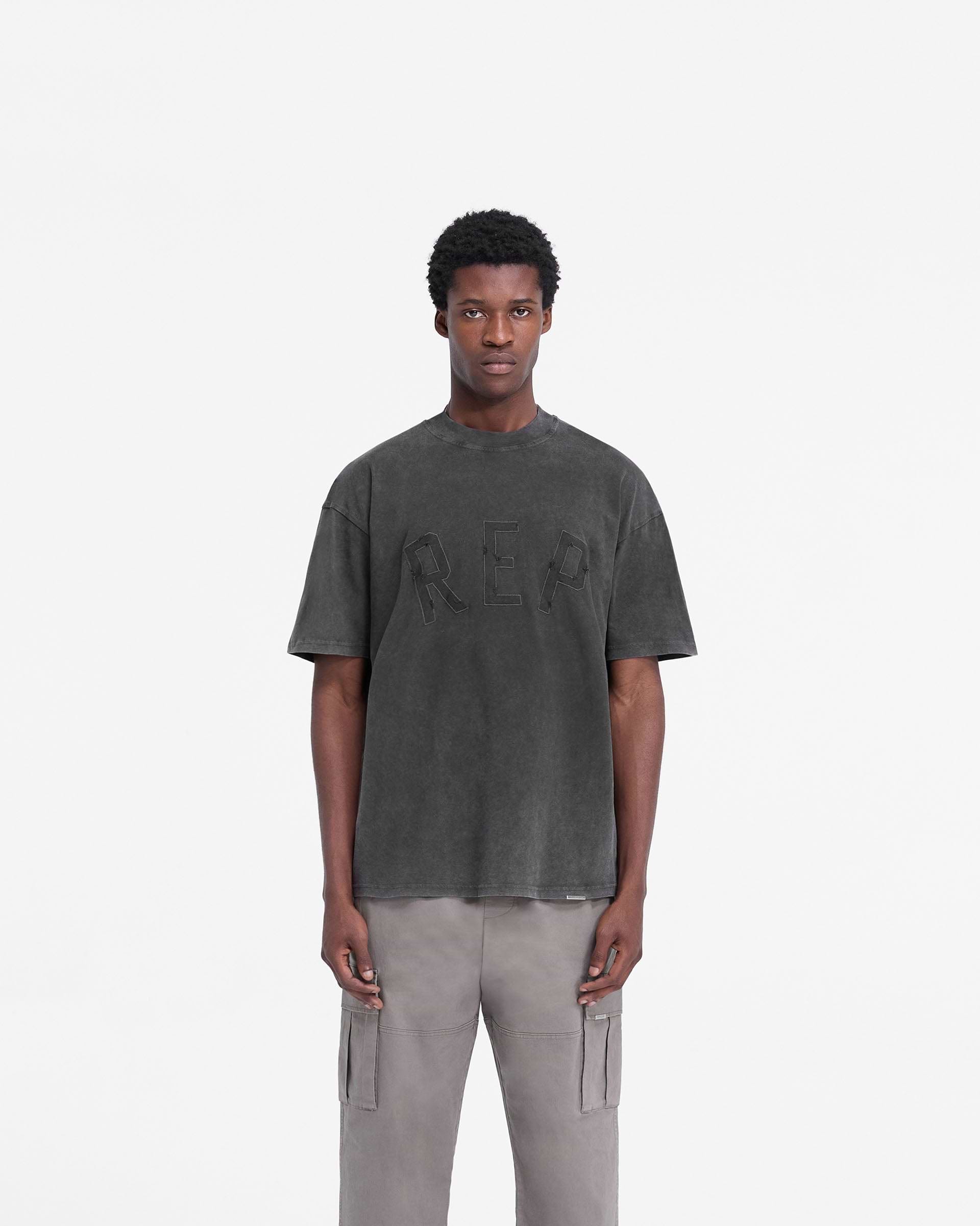 Man wearing a black t-shirt on a plain white background | Rep Applique T-Shirt in Vintage Black | Oversized t-shirt with distressed applique logo | FW24 T-Shirts | Represent Clo