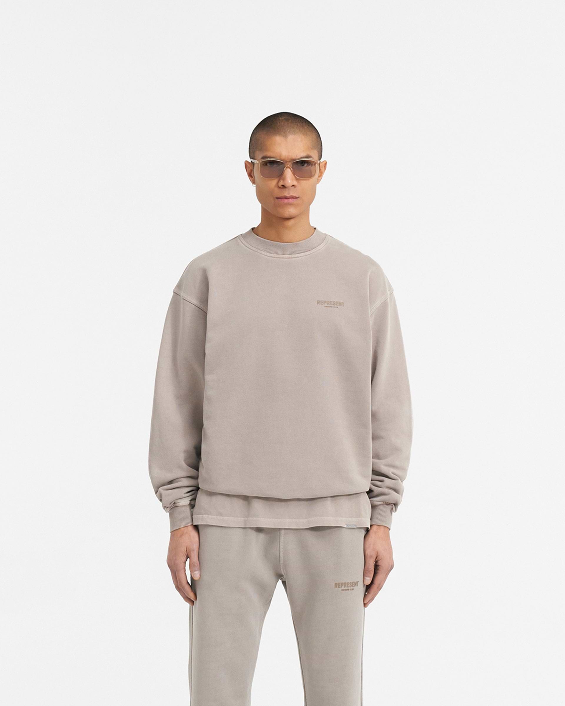 Man wearing a beige sweater on a plain white background | Represent Owners Club Sweater in Mushroom | Oversized crewneck sweater with ribbed trims | Owners Club Sweaters | Represent Clo