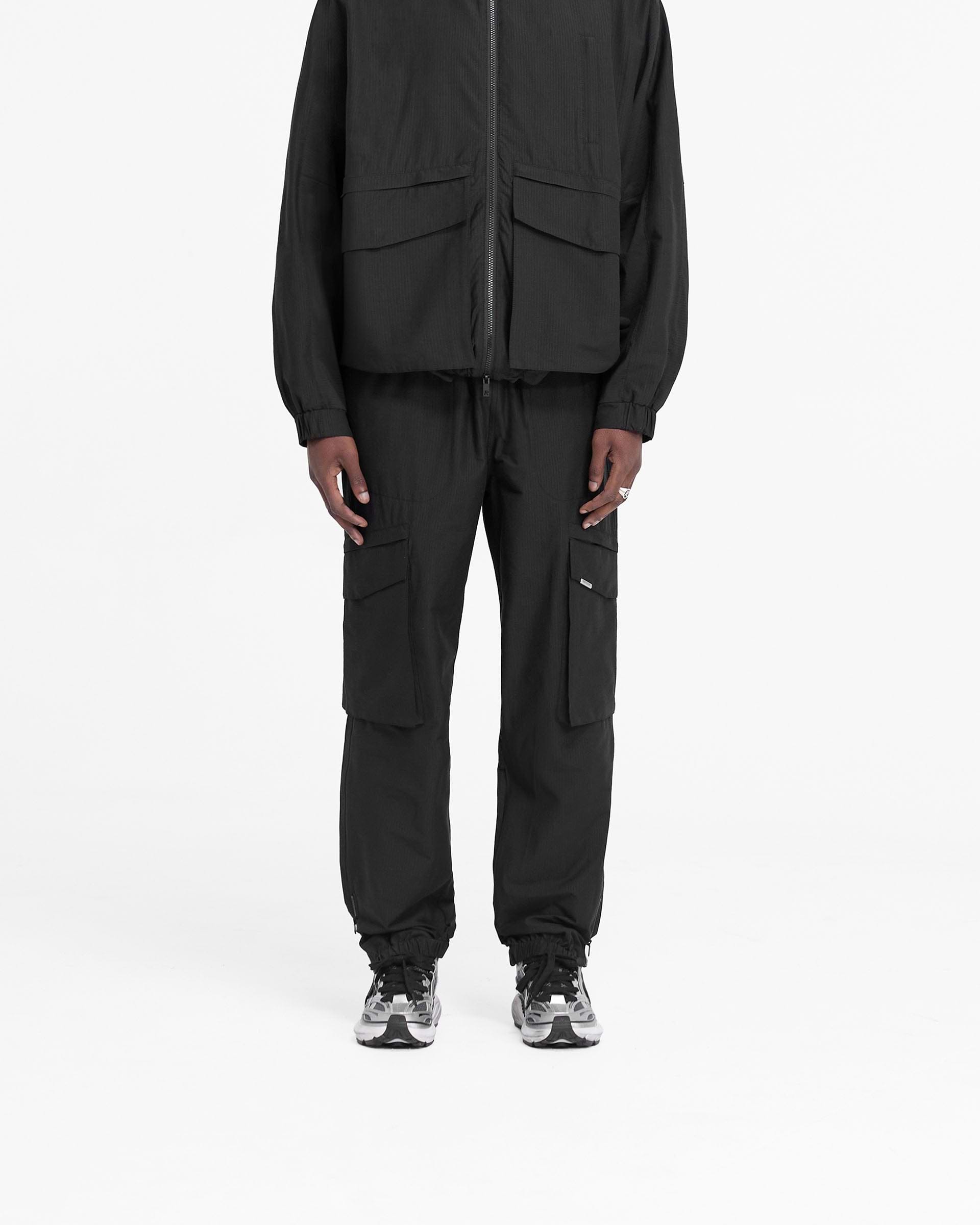 Man wearing black cargo pants on a plain white background | Tech Cargo Pant in Jet Black | Relaxed fit cargo pants with elasticated cuff and zip closure | FW24 Pants | Represent Clo