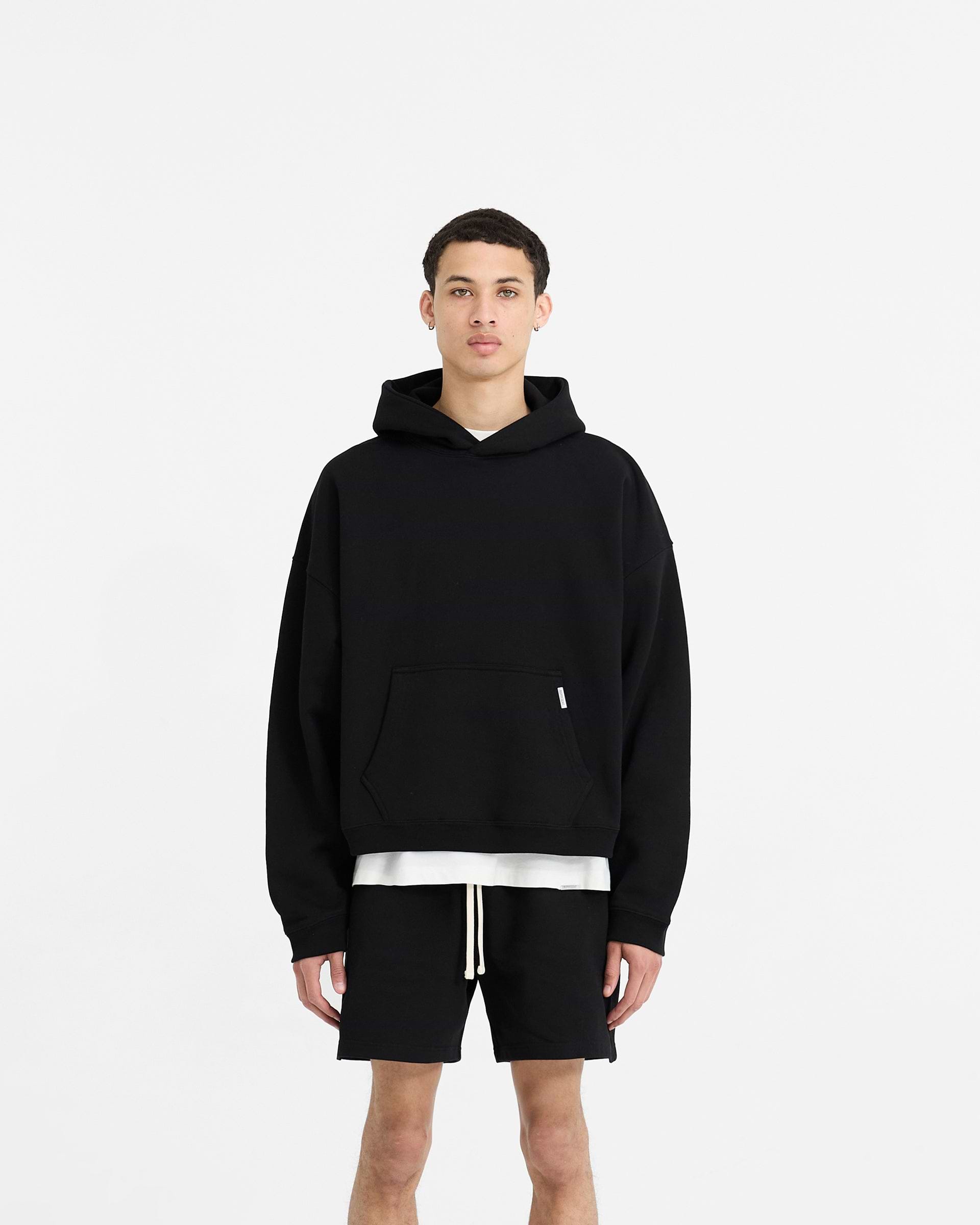 Man wearing a boxy black hoodie on a plain white background | Initial Boxy Hoodie in Black | Oversized cropped hoodie with dropped shoulders | Initial Hoodies | Represent Clo