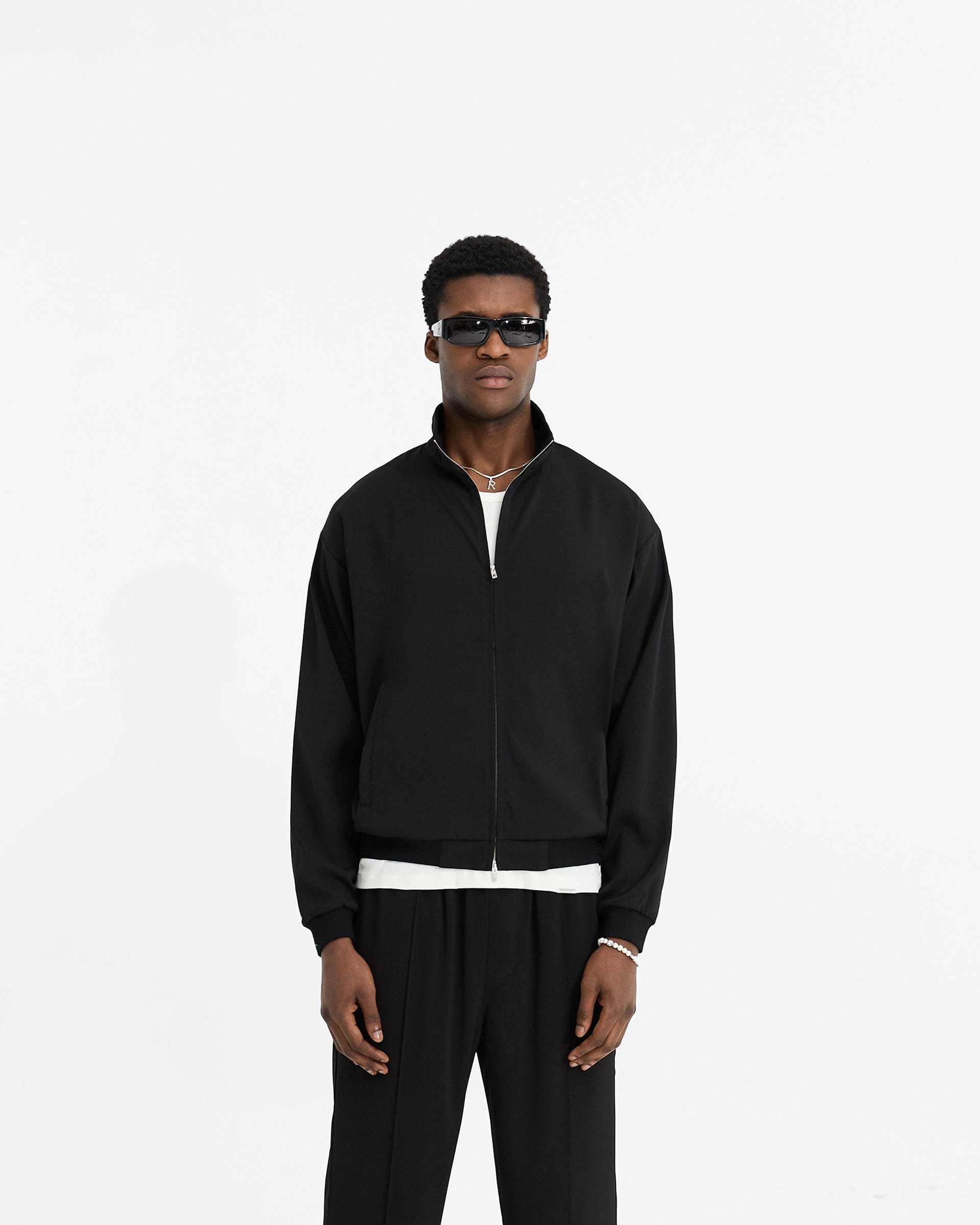 Man wearing a black track jacket on a plain white background | Initial Track Jacket in Black | Slightly oversized track jacket with welt pockets | Initial Outerwear | Represent Clo