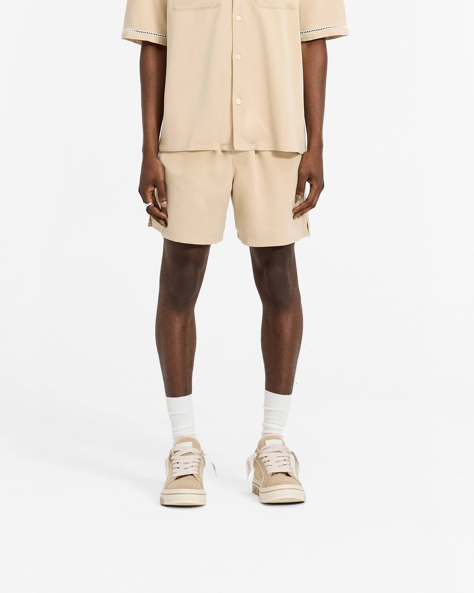 Man wearing latte brown relaxed fit shorts on a plain white background | Resort Shorts in Latte | Shorts with elasticated waistband and drawcord | SC24 Shorts | Represent Clo
