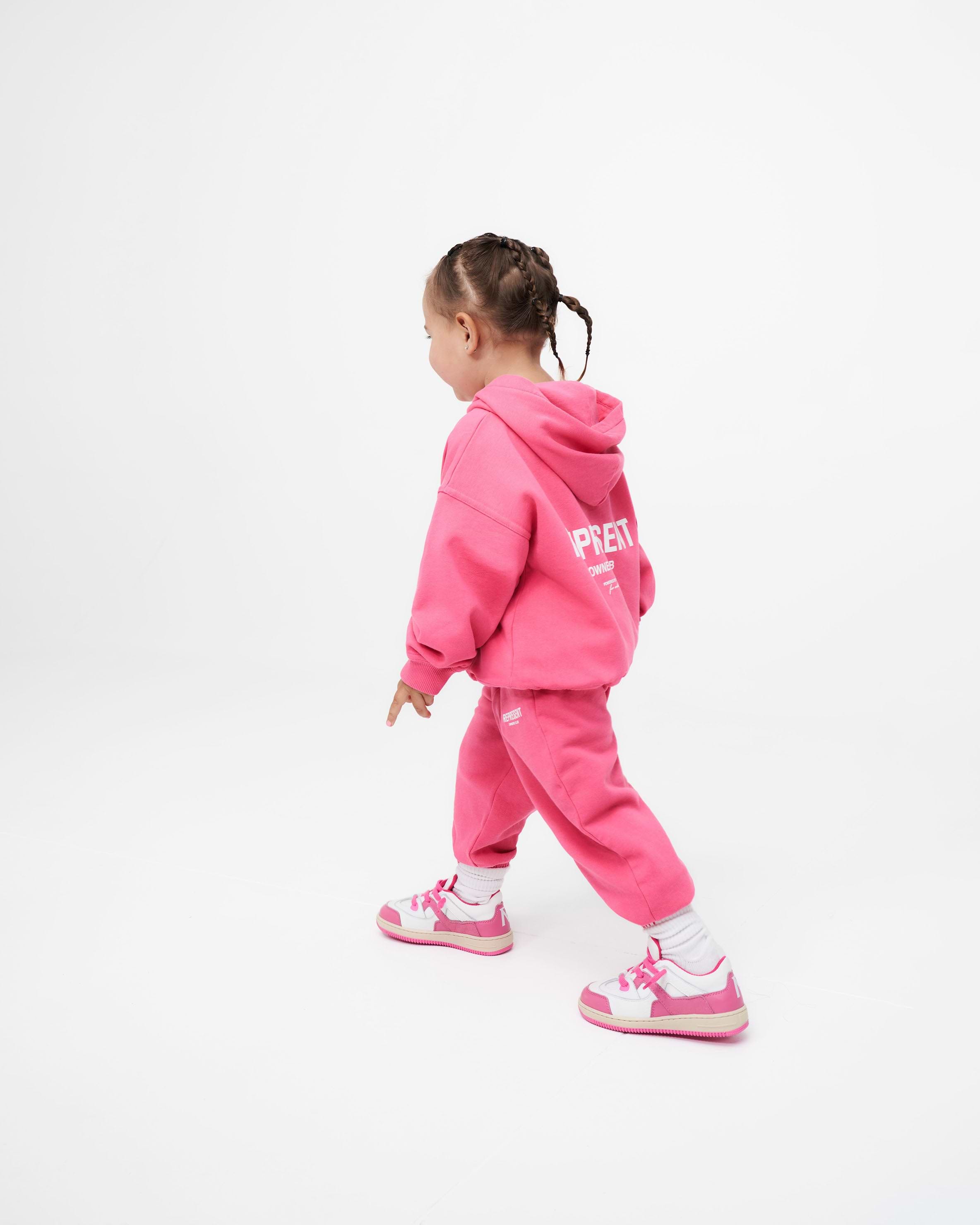 Child wearing pink sweatpants on a plain white background | Represent Mini Owners Club Sweatpants in Bubblegum Pink | Kids joggers with elasticated waistband | Owners Club Pants | Represent Clo