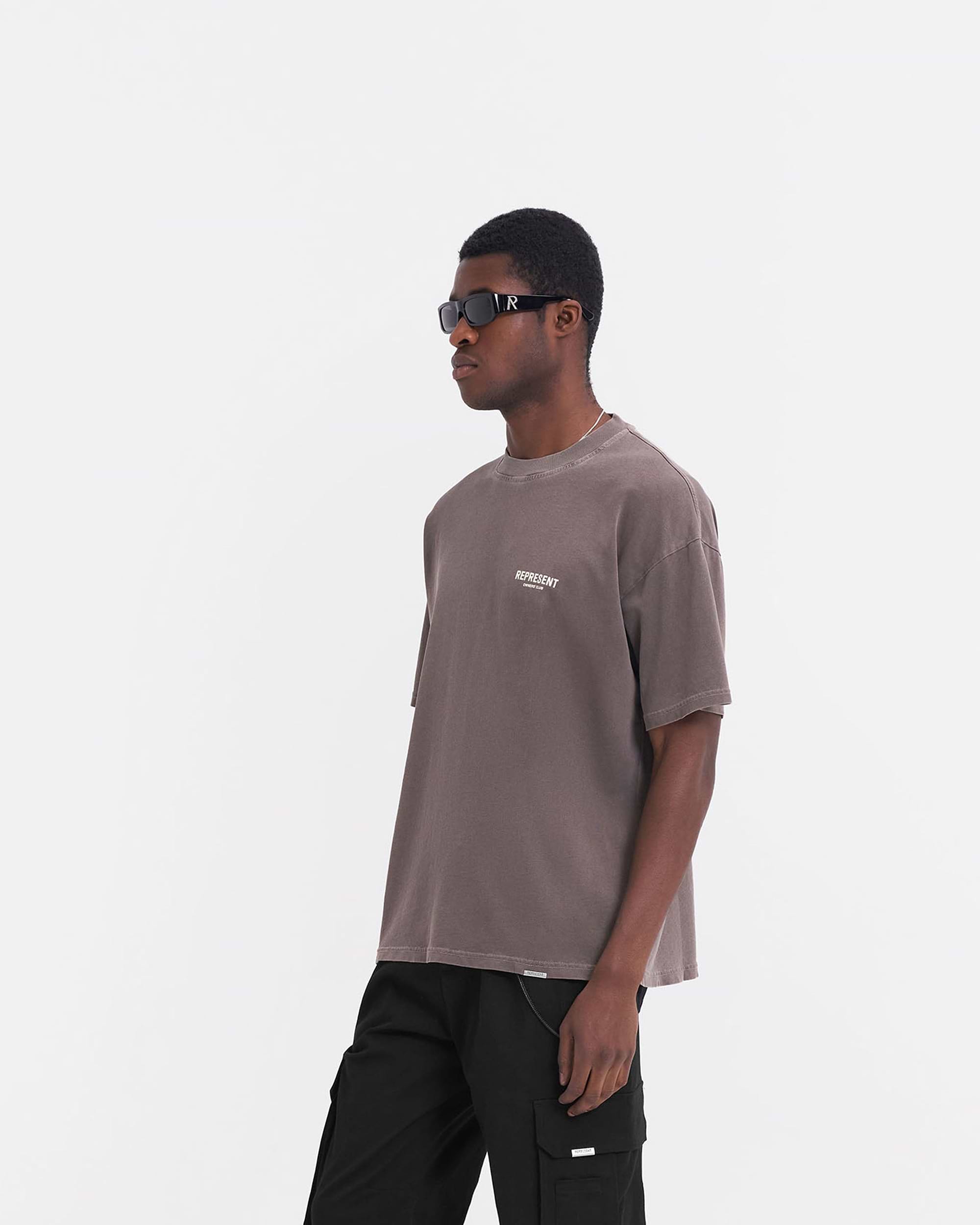 Man wearing an oversized grey t-shirt on a plain white background | Represent Owners Club T-Shirt in Fog | Screen printed short sleeve t-shirt with Owners Club branding | Owners Club T-Shirts | Represent Clo