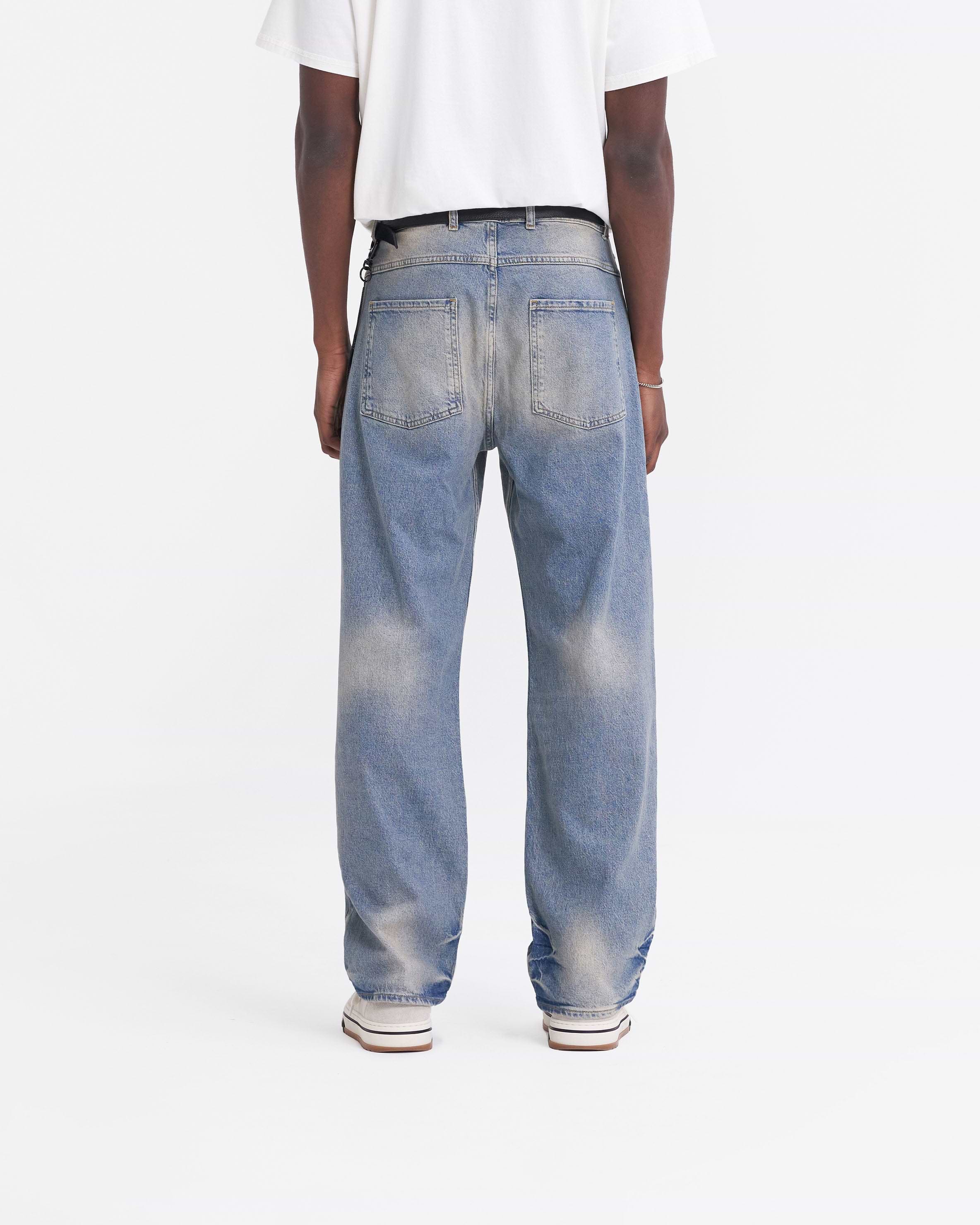 Man wearing blue baggy denim jeans on a plain white background | R3 Baggy Denim in Blue | Relaxed fit denim jeans with embroidered Initial | SS24 Denim | Represent Clo