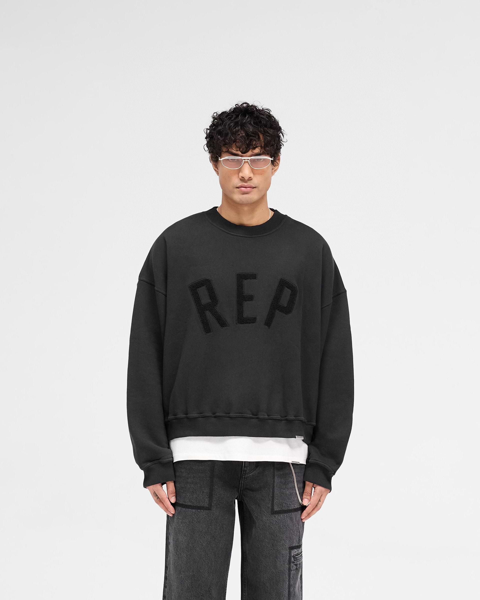 Man wearing a black sweater on a plain white background | Rep Applique Sweater in Off Black | Boxy fit sweater with textured Rep applique | SS25 Sweaters | Represent Clo