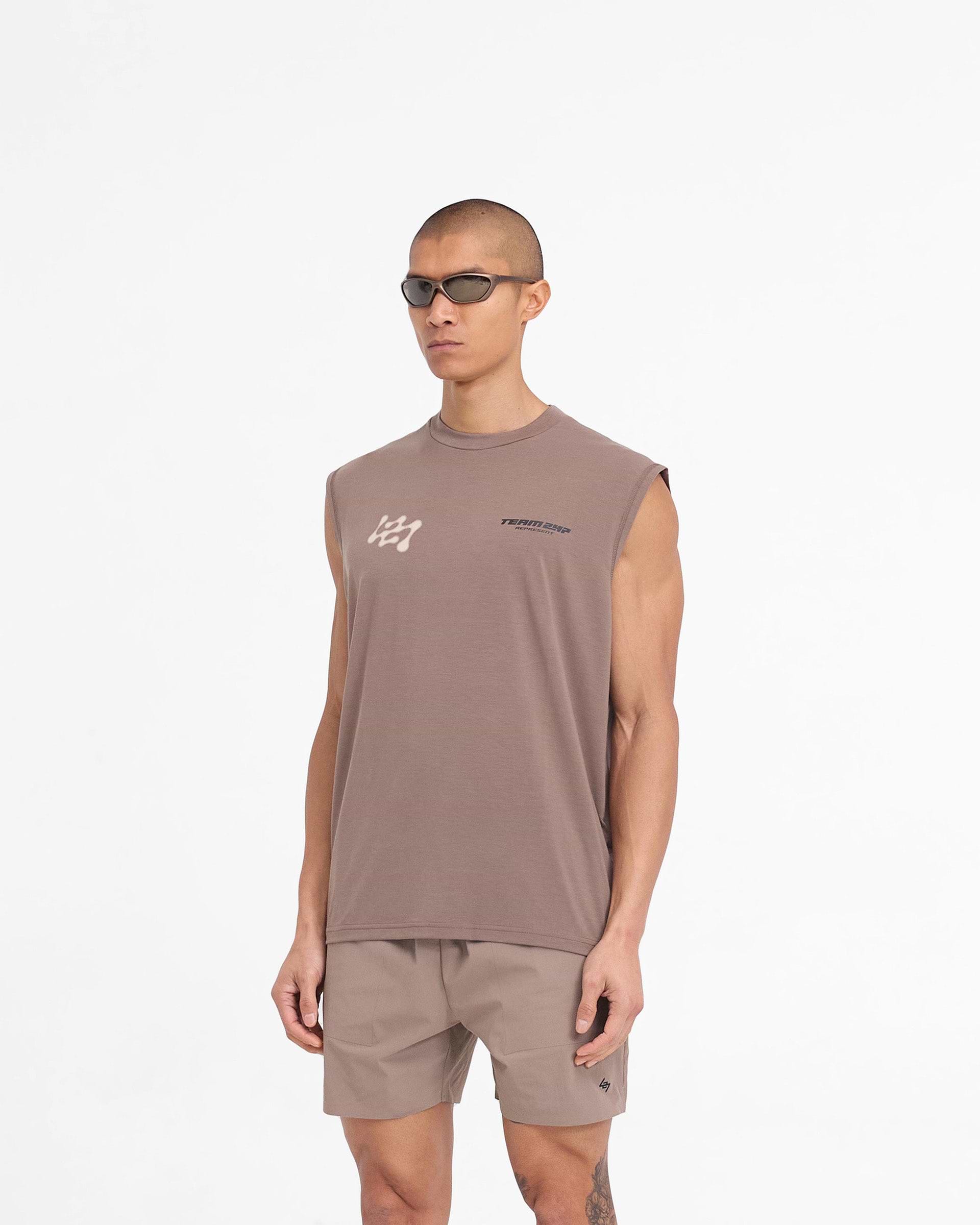 Man wearing a brown oversized tank top on a plain white background | 247 Future Terrains Oversized Tank in Umber | Oversized tank top with Future Terrains branding | 247 T-Shirts | Represent Clo