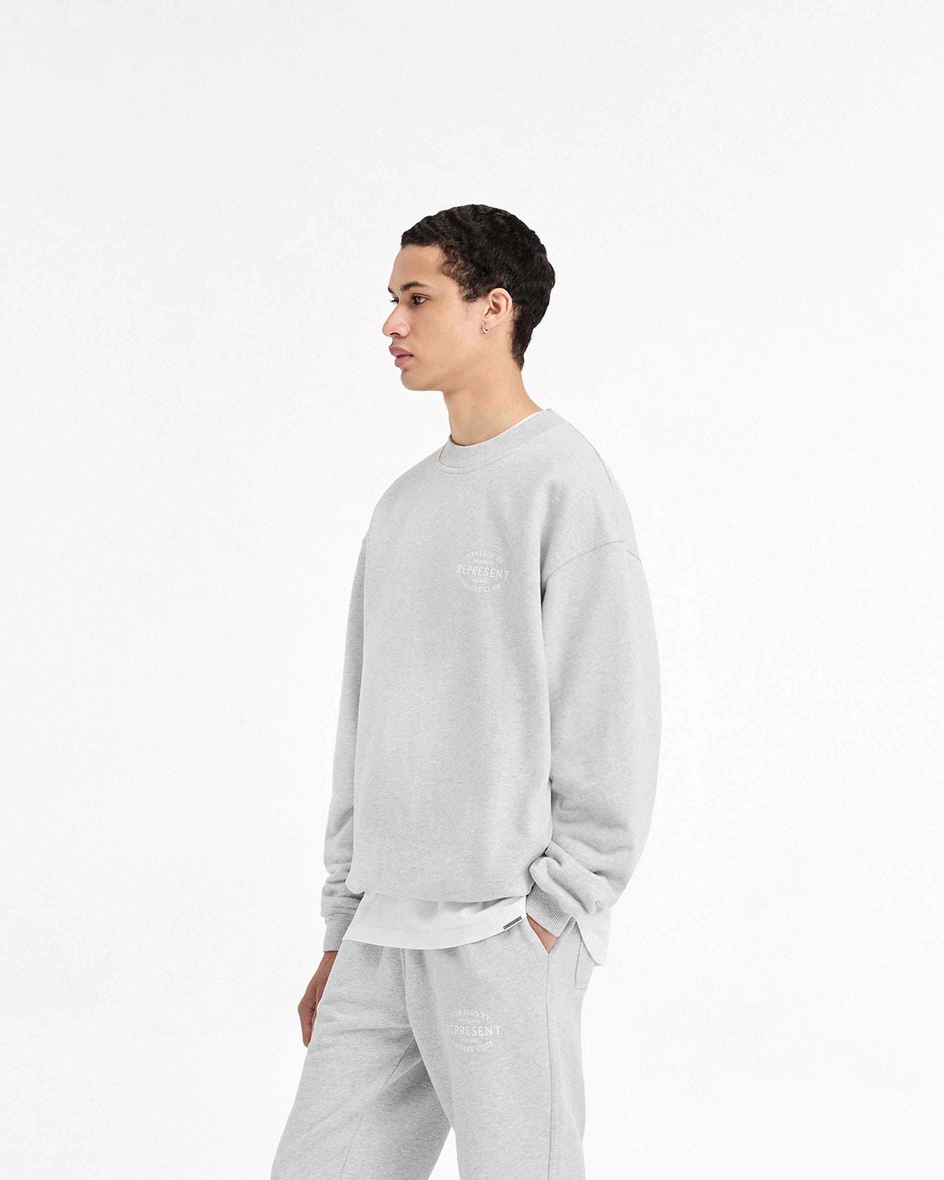Man wearing a grey sweater on a plain white background | Represent Owners Club Stamp Sweater in Ash Grey | Sweater with ribbed hem and cuffs | Owners Club Sweaters | Represent Clo
