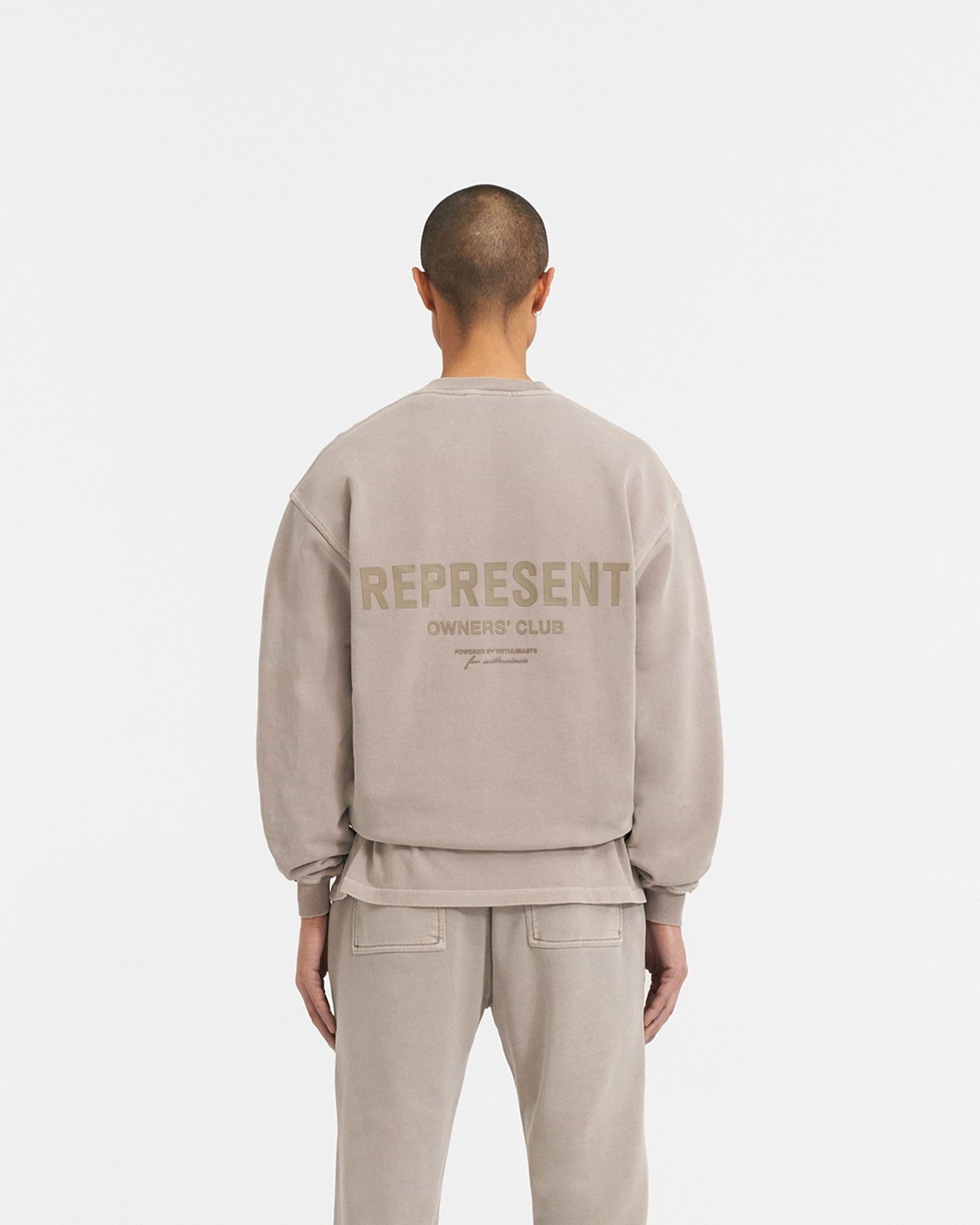 Man wearing an oversized grey sweater on a plain white background | Represent Owners Club Sweater in Mushroom | Crewneck sweater with high build branding | Owners Club Sweaters | Represent Clo
