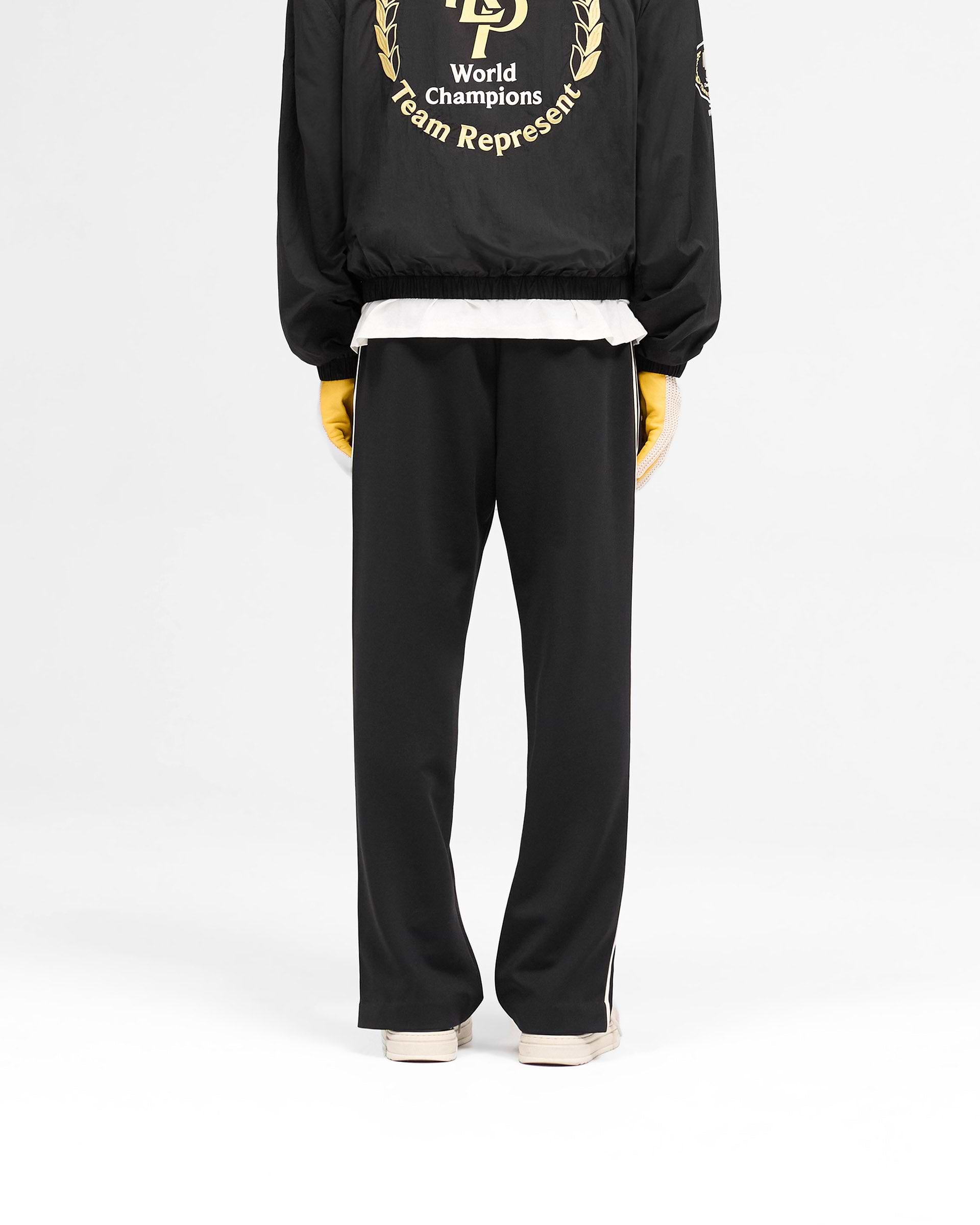 Man wearing black tailored track pants on a plain white background | Tailored Track Pant in Jet Black | Tailored pants with elasticated waistband and zip detail | SS25 Pants | Represent Clo