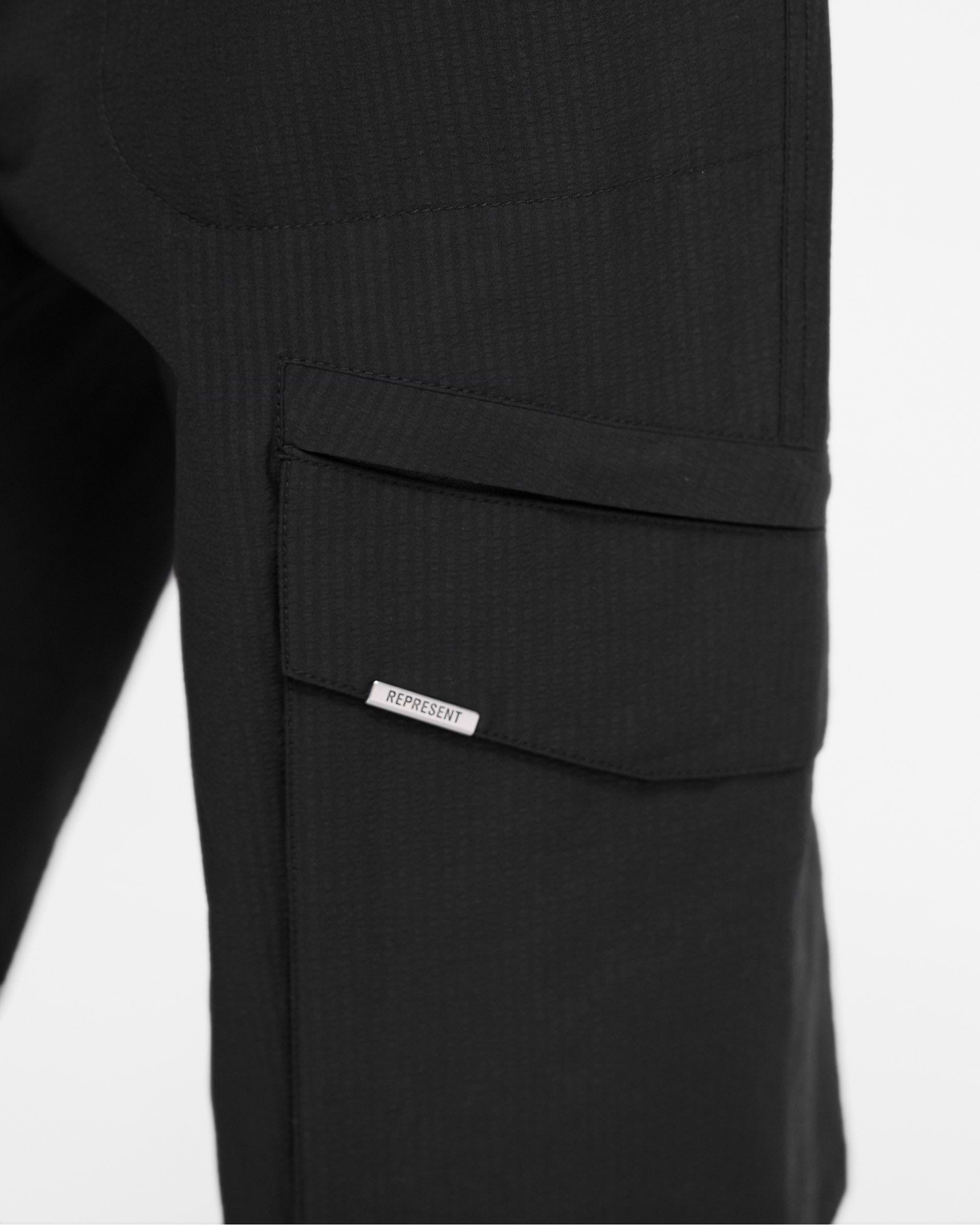 Man wearing black cargo pants on a plain white background | Tech Cargo Pant in Jet Black | Cargo pants with elasticated waistband and diagonal pockets | FW24 Pants | Represent Clo