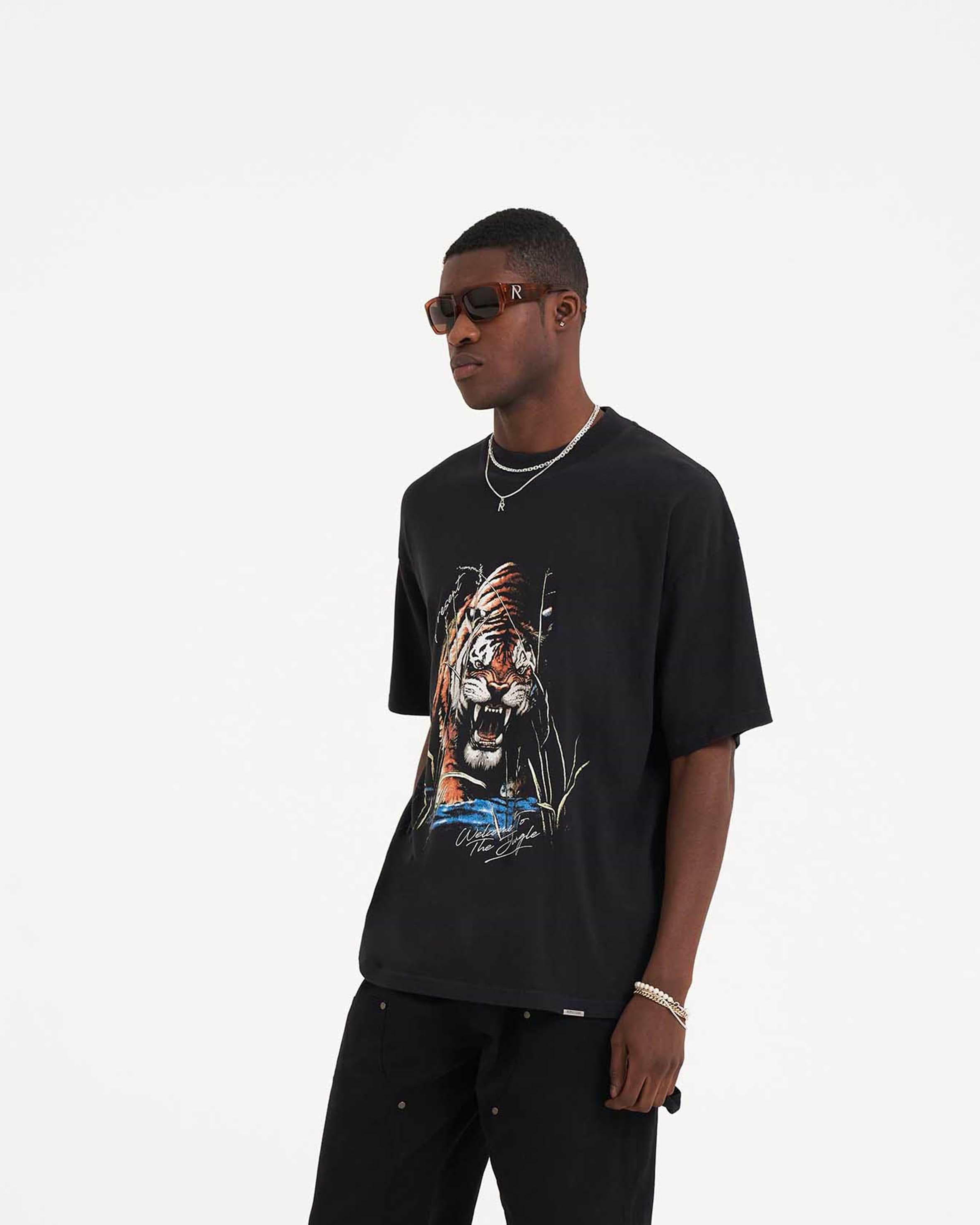Man wearing an off black graphic t-shirt on a plain white background | Welcome To The Jungle T-Shirt in Off Black | Short sleeve oversized cotton t-shirt with graphic | SS23 T-Shirts | Represent Clo