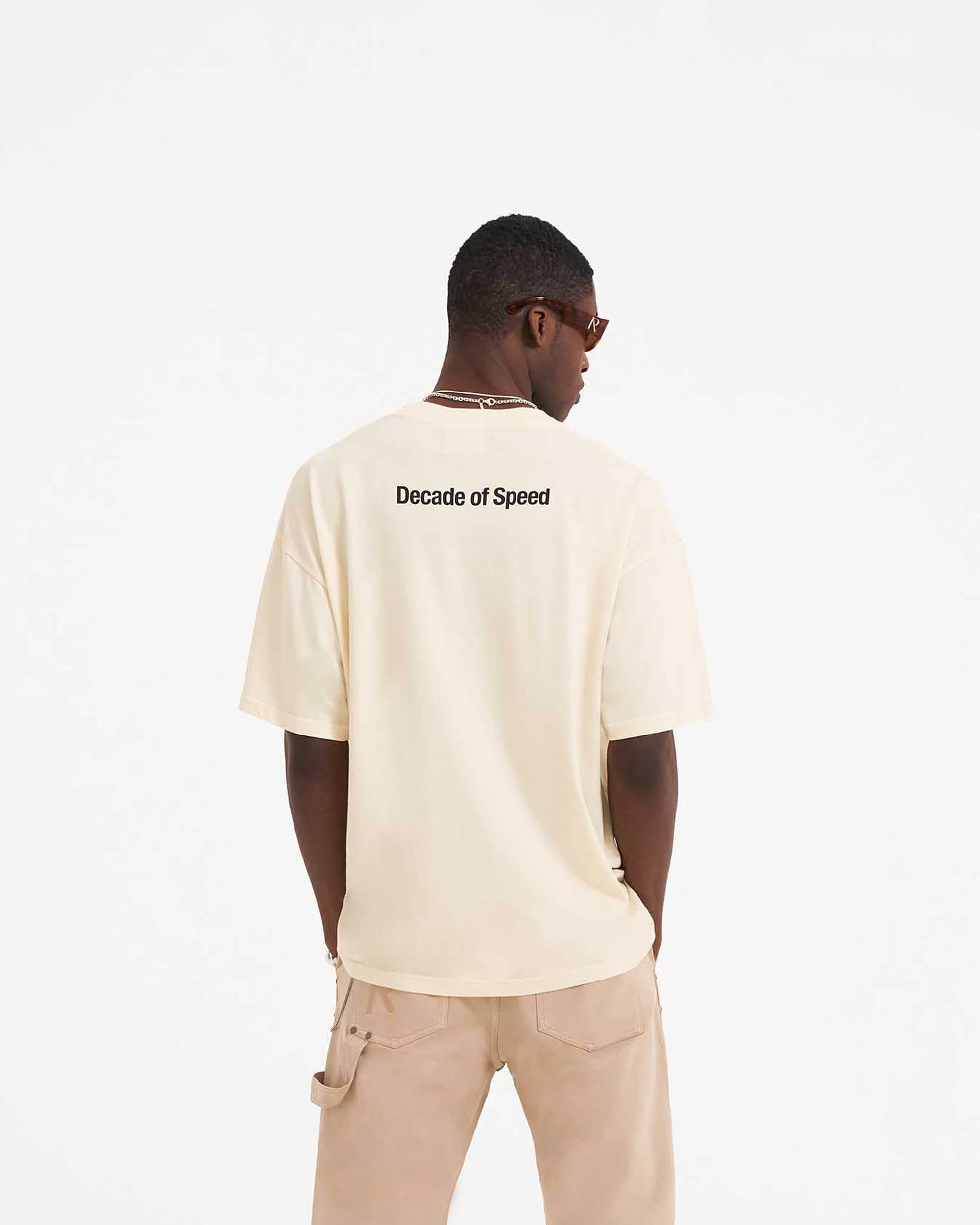 Man wearing a cream t-shirt on a plain white background | Decade Of Speed T-Shirt in Cream | Oversized fit short sleeve graphic t-shirt | SS23 T-Shirts | Represent Clo