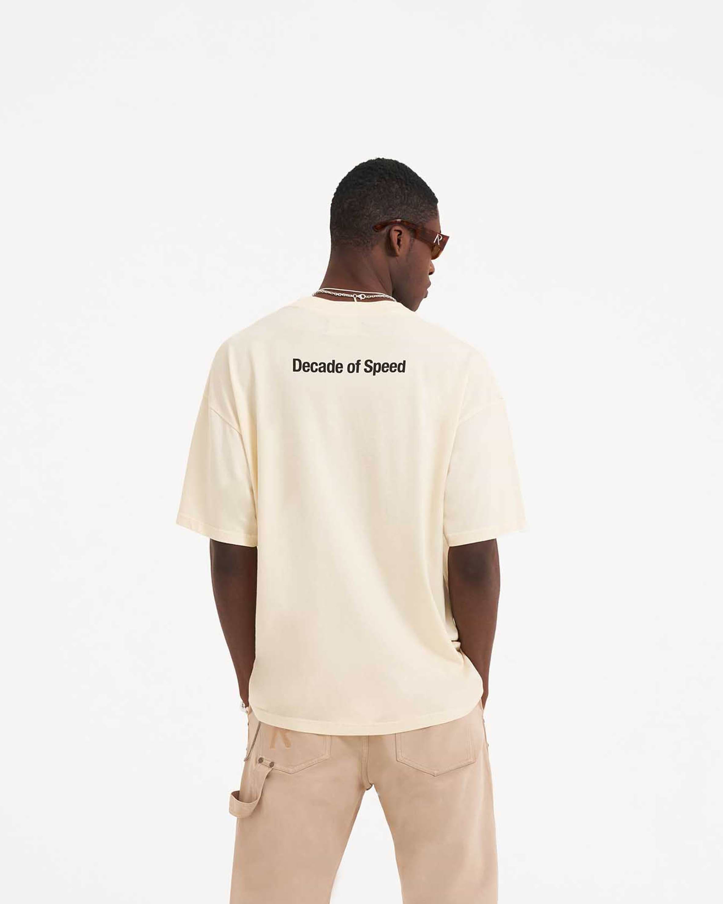 Man wearing a cream t-shirt on a plain white background | Decade Of Speed T-Shirt in Cream | Oversized fit short sleeve graphic t-shirt | SS23 T-Shirts | Represent Clo