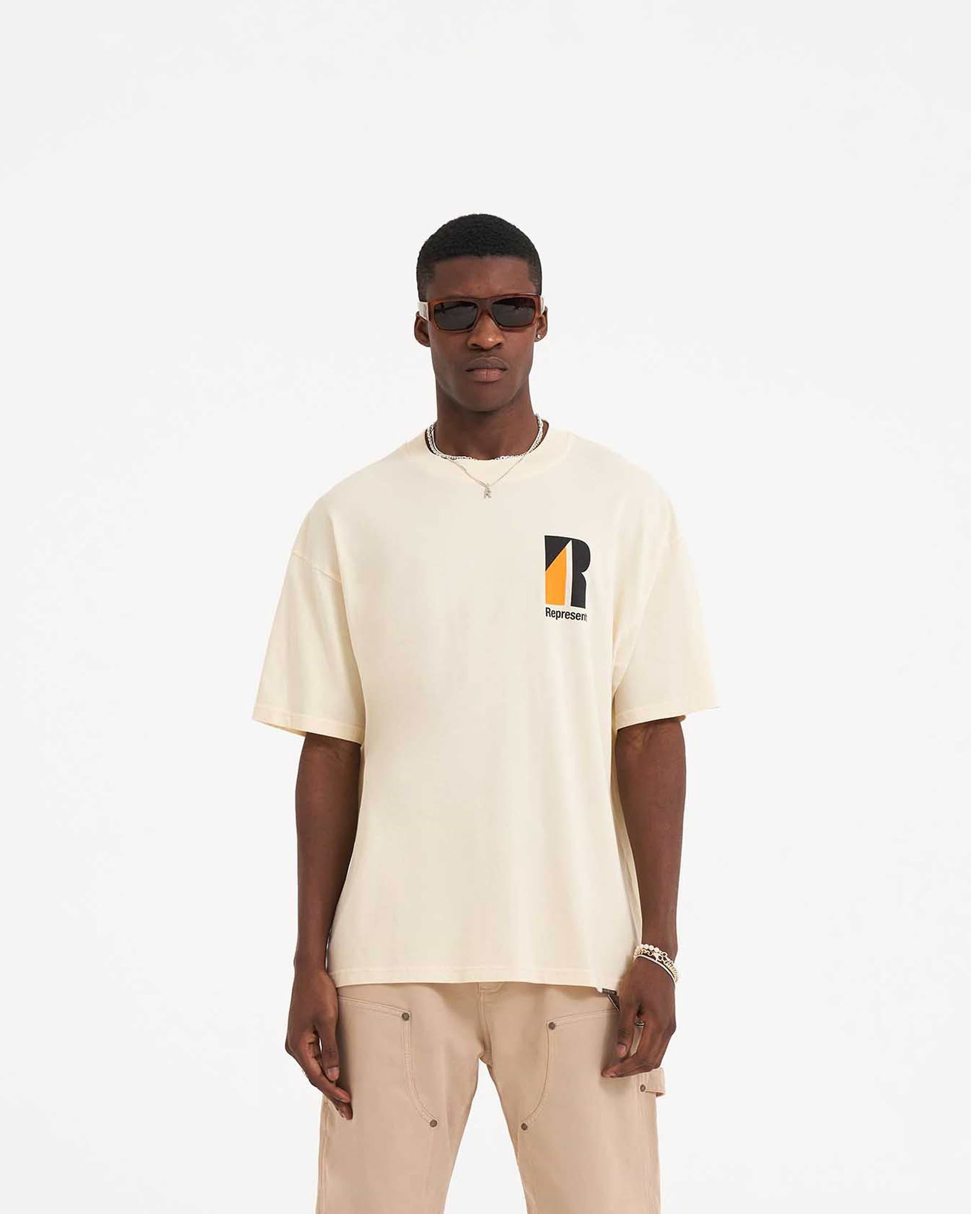 Man wearing a cream t-shirt on a plain white background | Decade Of Speed T-Shirt in Cream | Oversized graphic t-shirt with ribbed crewneck | SS23 T-Shirts | Represent Clo