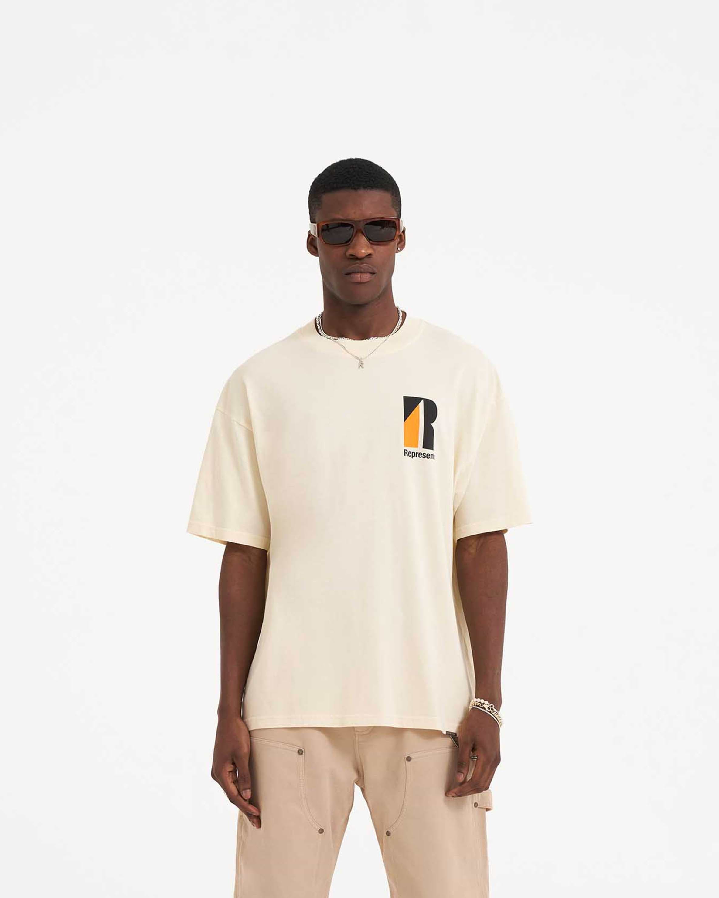 Man wearing a cream t-shirt on a plain white background | Decade Of Speed T-Shirt in Cream | Oversized graphic t-shirt with ribbed crewneck | SS23 T-Shirts | Represent Clo