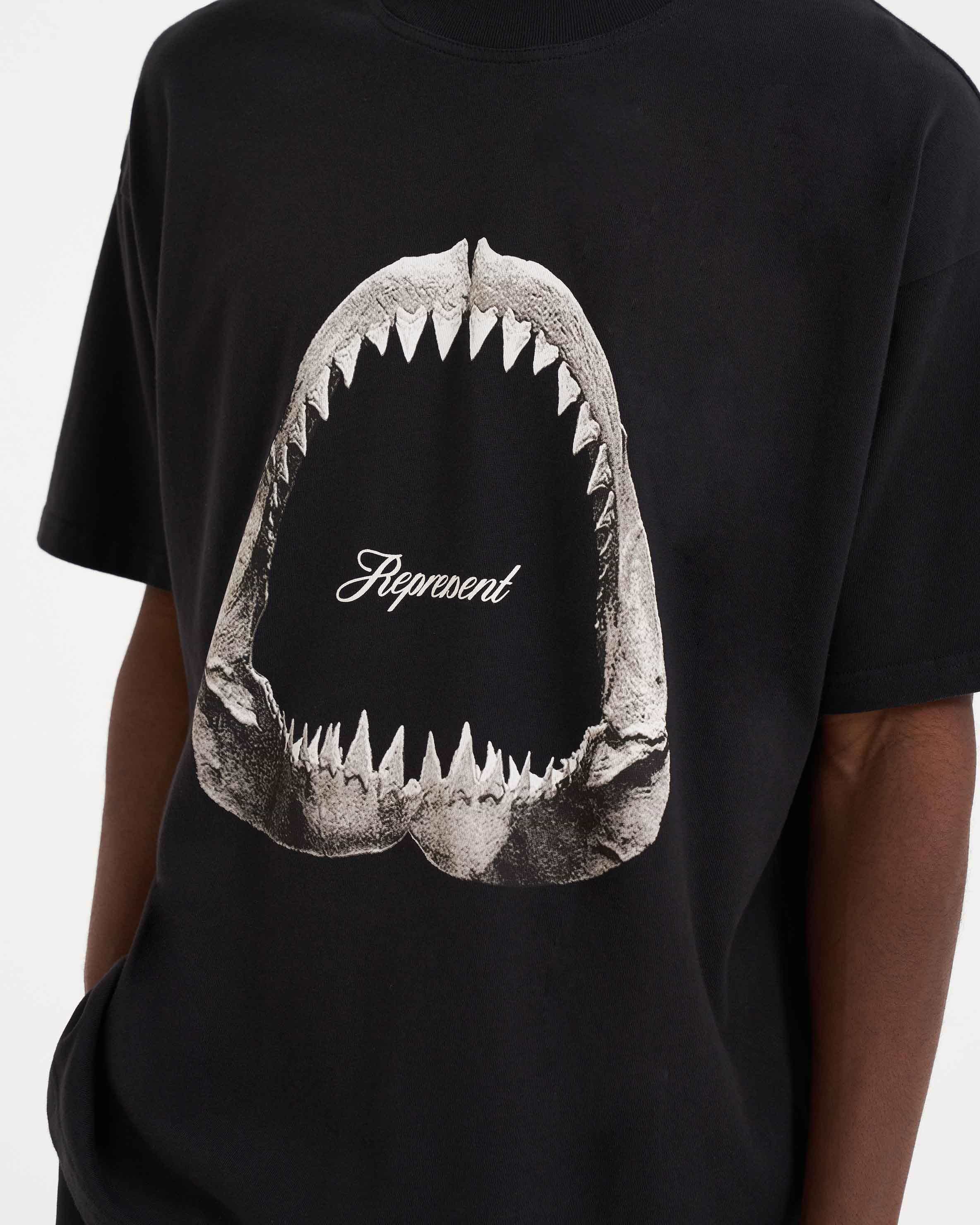 Man wearing an off black graphic t-shirt on a plain white background | Shark Jaws T-Shirt in Off Black | Oversized t-shirt with ribbed crewneck and shark jaws graphic | SS23 T-Shirts | Represent Clo