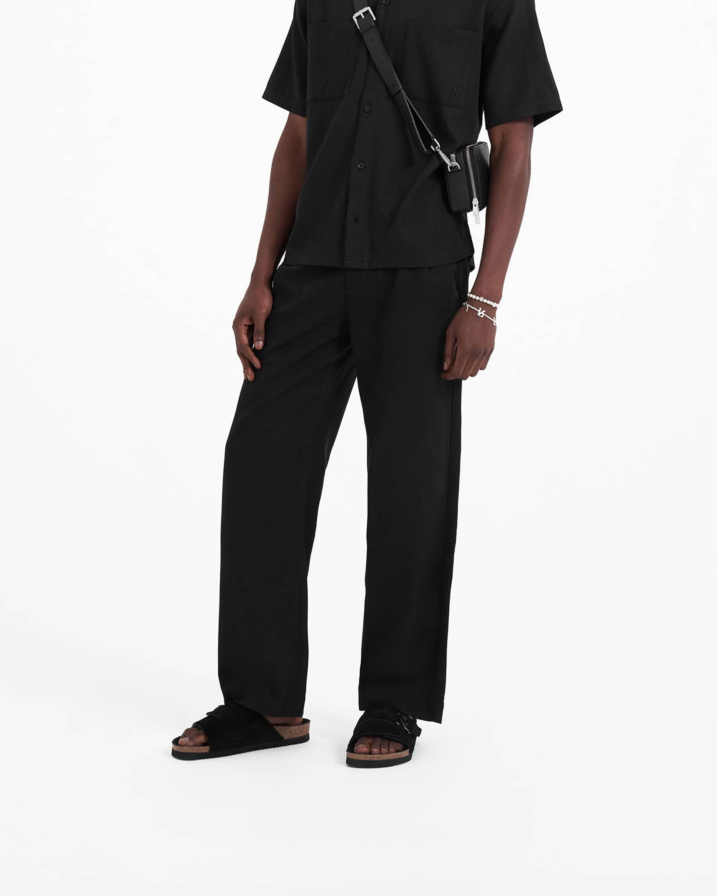 Man wearing black relaxed fit pants on a plain white background | Yacht Pant in Black | Pants with hybrid elasticated waistband | SC23 Pants | Represent Clo