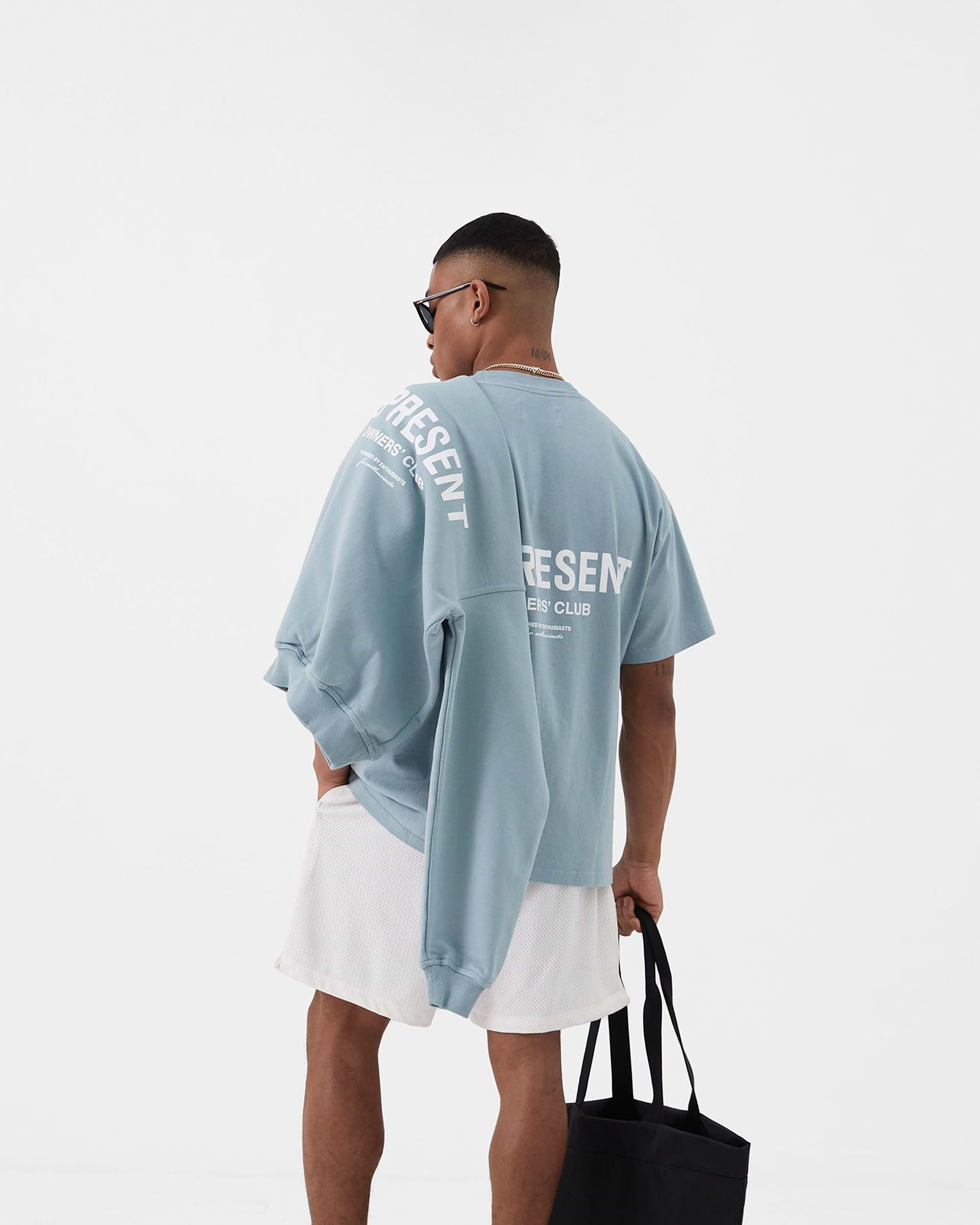 Man wearing a blue t-shirt on a plain white background | Represent Owners Club T-Shirt in Powder Blue | Oversized t-shirt with ribbed crewneck and graphic branding | Owners Club T-Shirts | Represent Clo