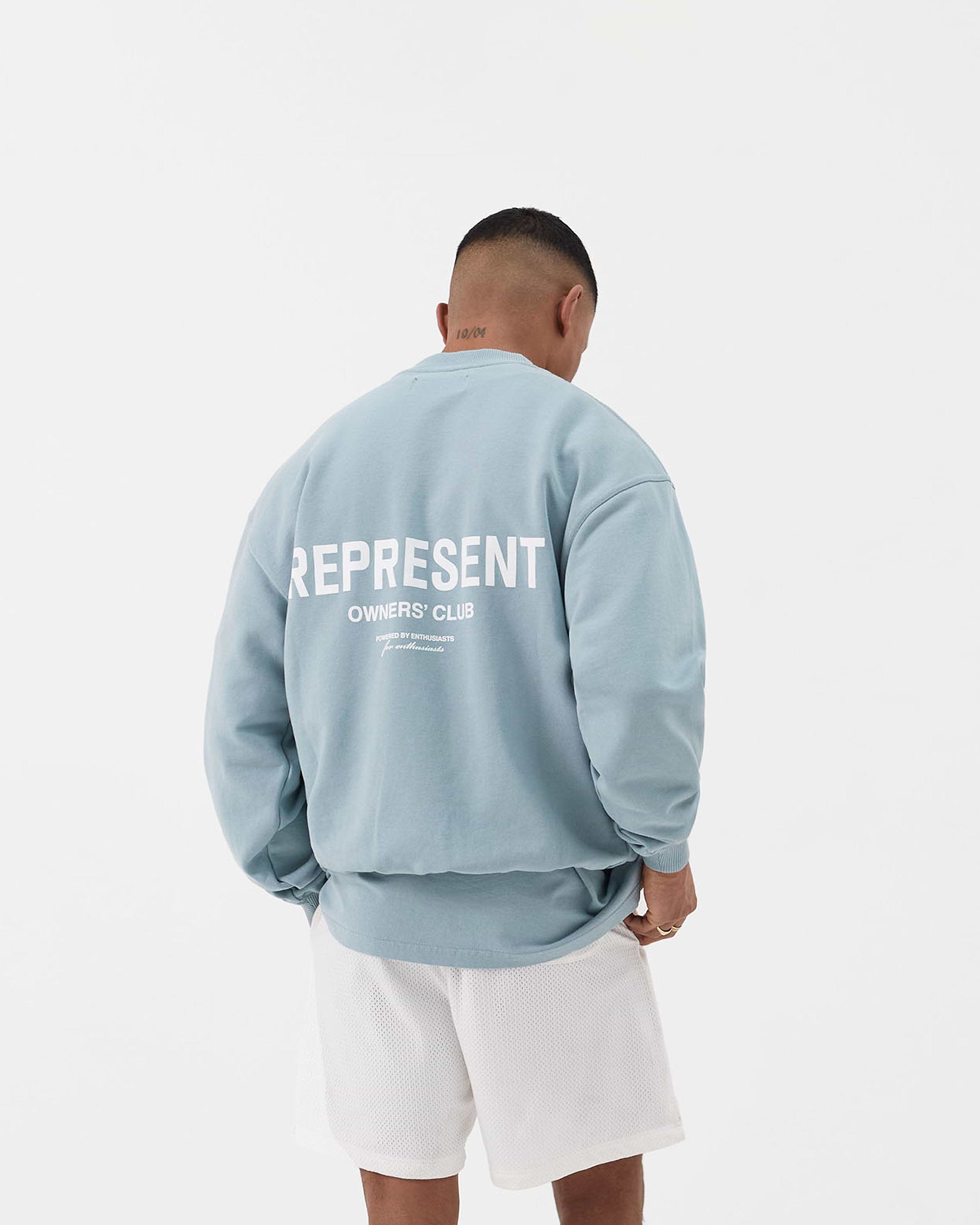 Man wearing a blue sweater on a plain white background | Represent Owners Club Sweater in Powder Blue | Oversized fit crewneck sweater with ribbed trims | Owners Club Sweaters | Represent Clo