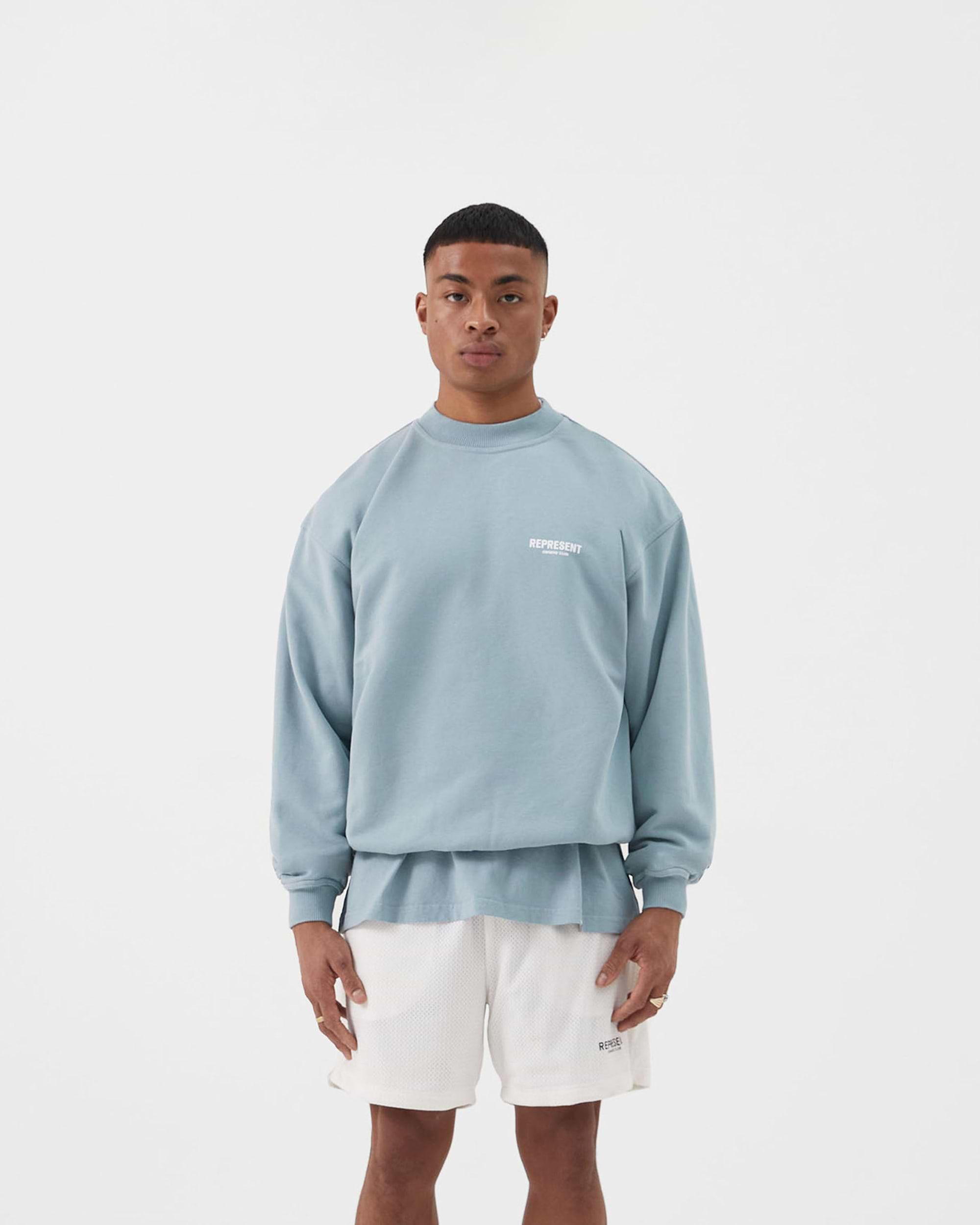 Man wearing an oversized blue sweater on a plain white background | Represent Owners Club Sweater in Powder Blue | Heavy weight jersey cotton crewneck sweater | Owners Club Sweaters | Represent Clo