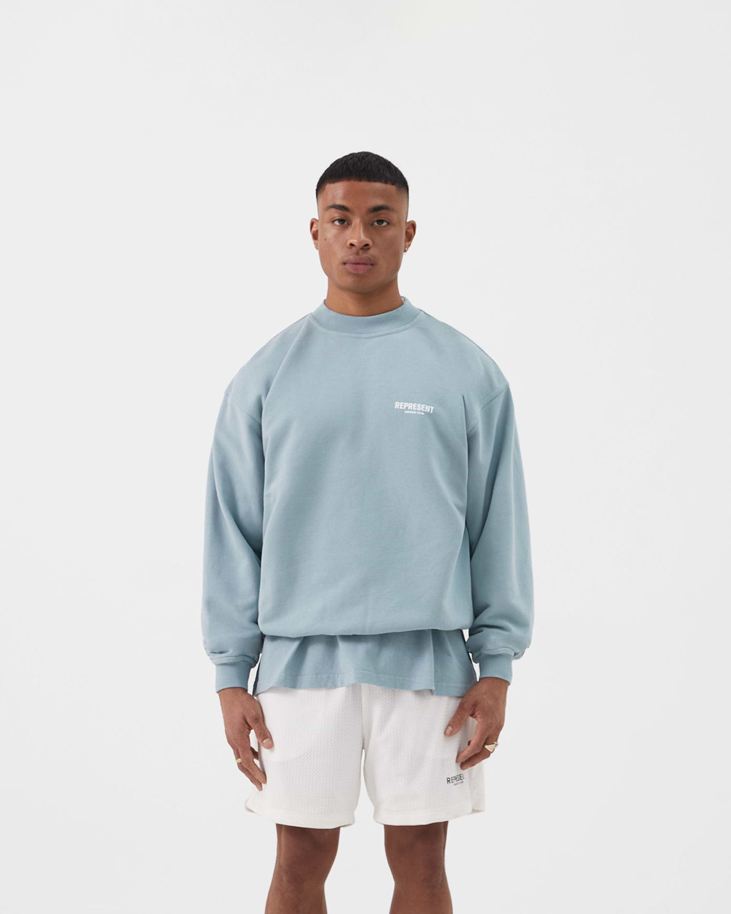 Man wearing an oversized blue sweater on a plain white background | Represent Owners Club Sweater in Powder Blue | Heavy weight jersey cotton crewneck sweater | Owners Club Sweaters | Represent Clo